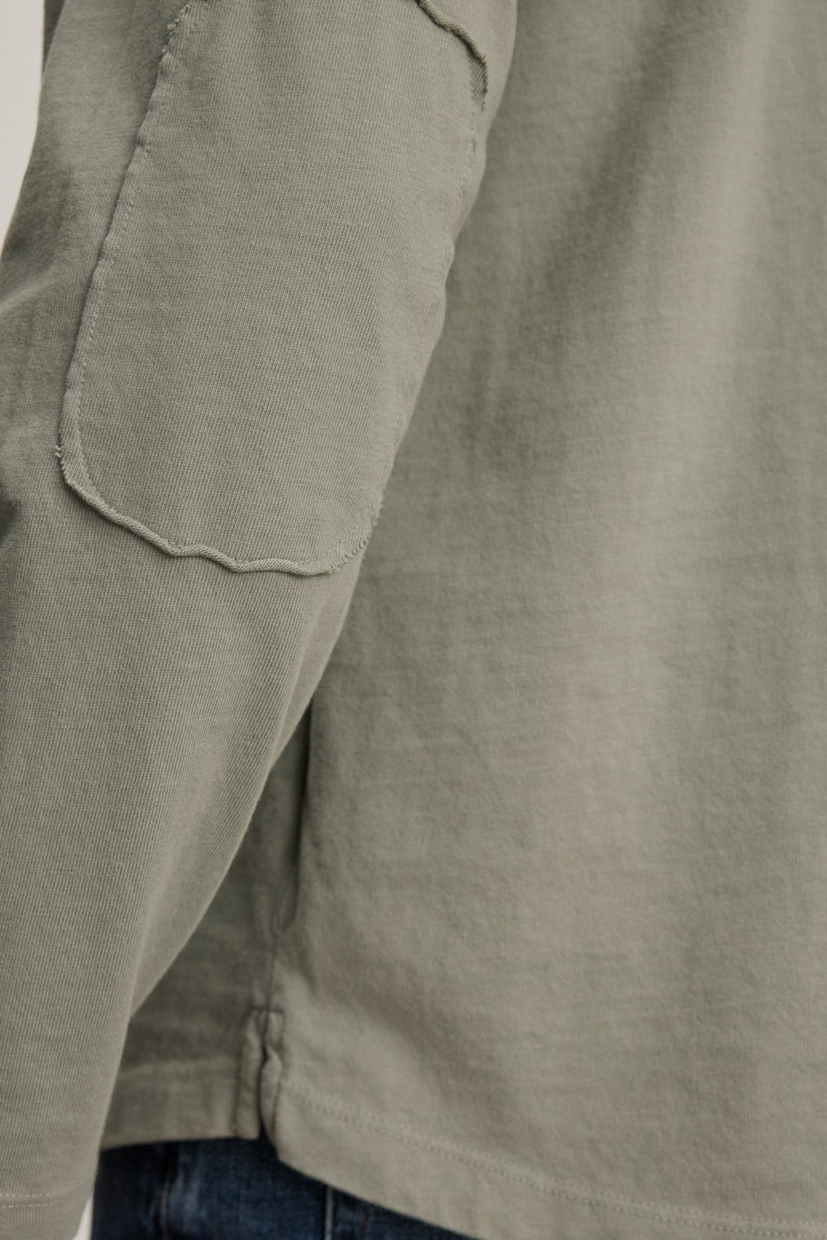   Close-up of a person in the Velvet by Graham & Spencer SLATER TEE, an olive-green long-sleeve crafted from structured pima cotton with a sleeve pocket, paired with blue jeans for a versatile look. 