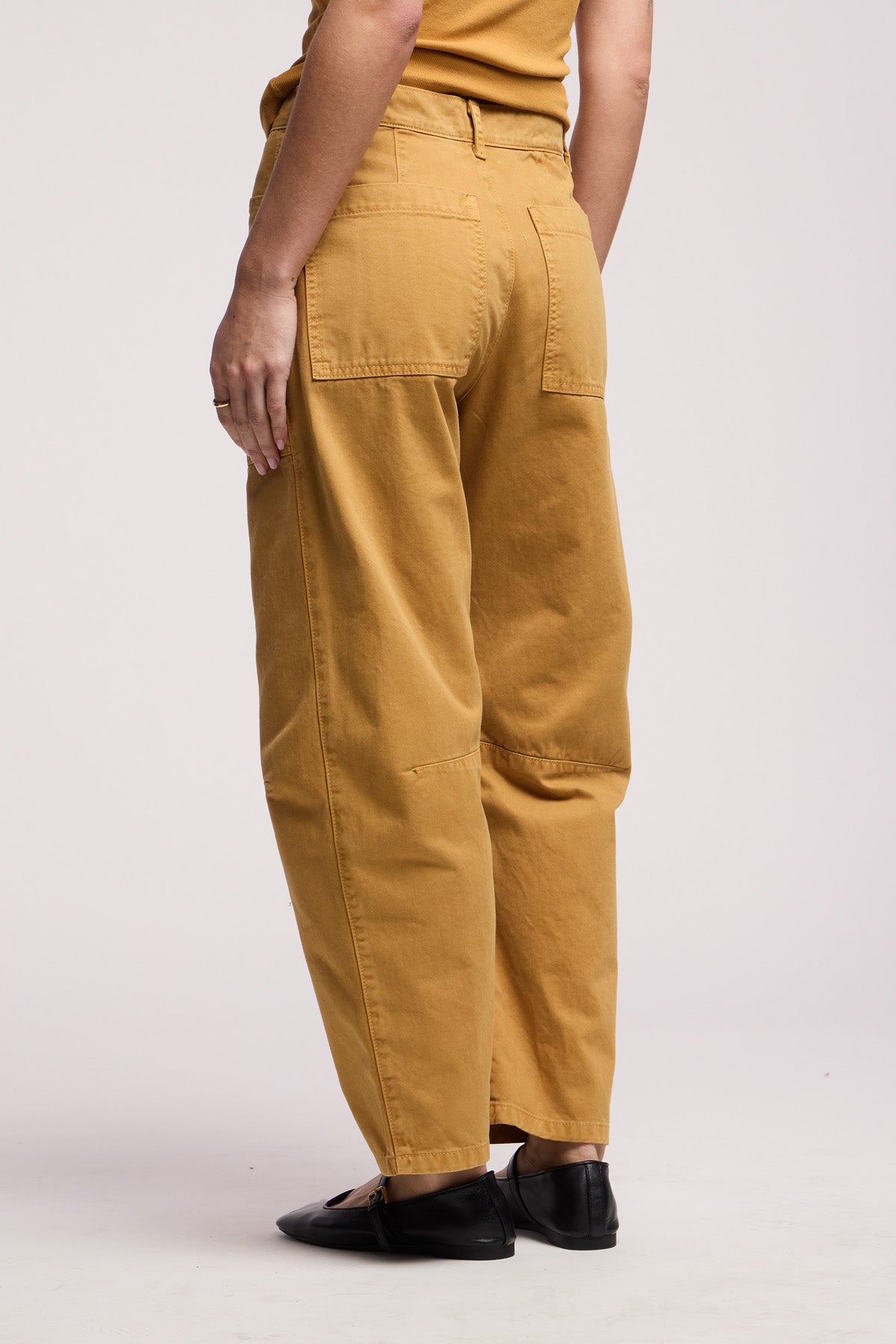 A person wearing the BRYLIE PANT by Velvet by Graham & Spencer—a mustard yellow cotton twill trouser with utilitarian patch pockets—and black shoes, stands against a plain light background.-41374540267713