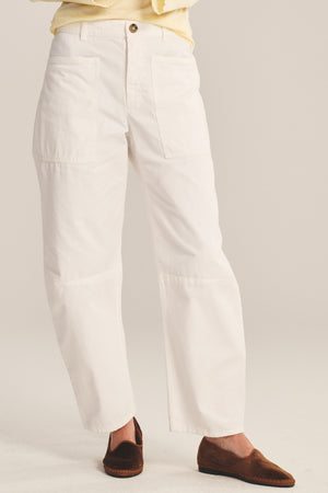 A person wears the BRYLIE PANT by Velvet by Graham & Spencer—white, straight-leg cotton twill trousers with utilitarian patch pockets—paired with brown slip-on shoes, standing against a neutral background.