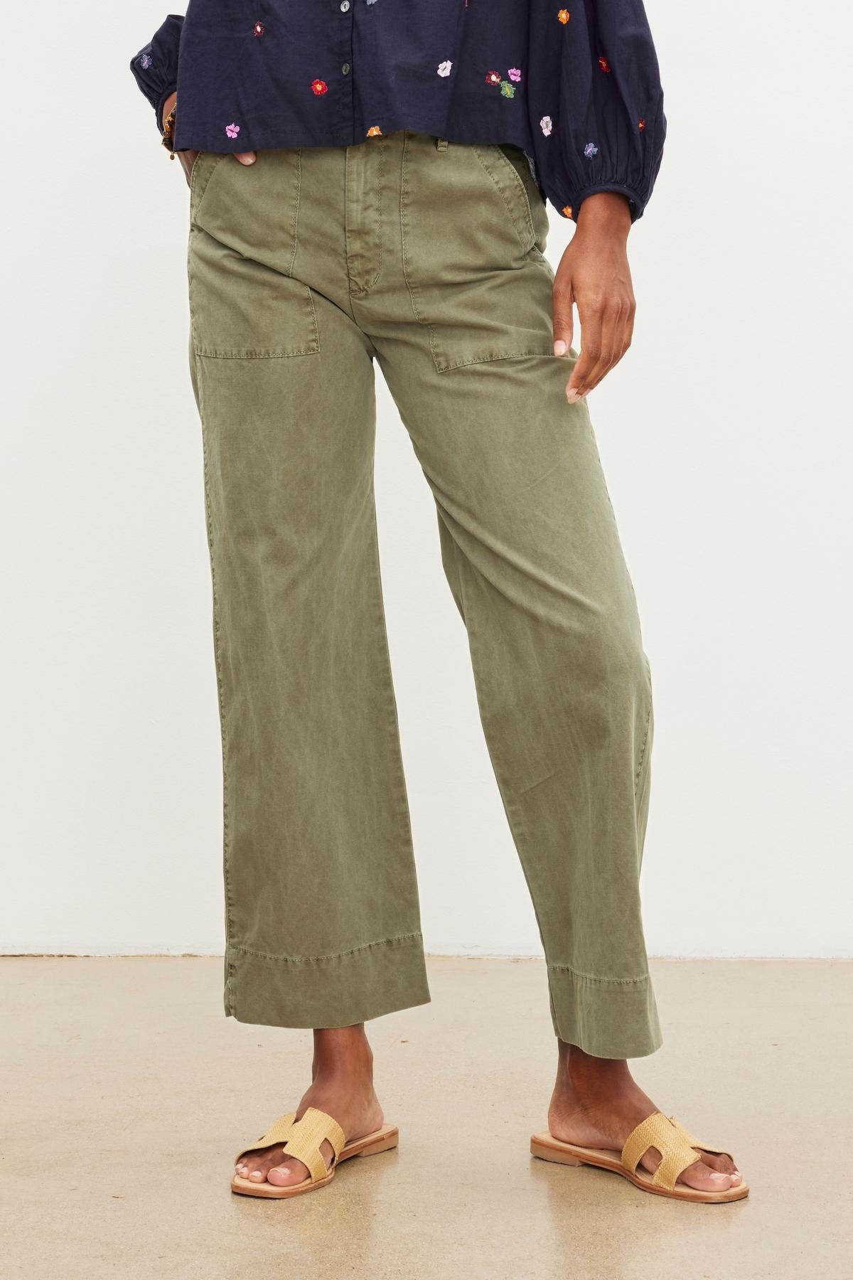 Person standing in Velvet by Graham & Spencer's MYA COTTON CANVAS PANT and sandals, with a focus on the lower half of their body against a neutral background.-37535283478721