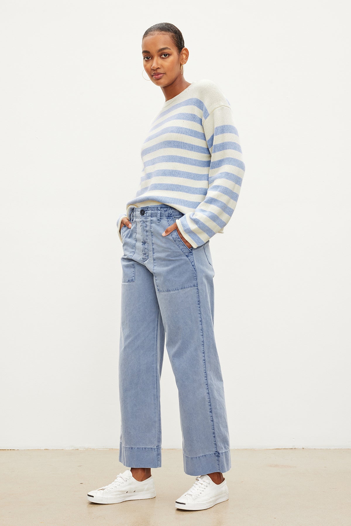   The model is wearing MYA COTTON CANVAS PANTS by Velvet by Graham & Spencer in blue and white stripes, paired with a striped sweater and jeans. 