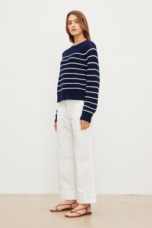 The model is wearing a CHAYSE STRIPED CREW NECK SWEATER by Velvet by Graham & Spencer with a relaxed silhouette and white wide leg pants.