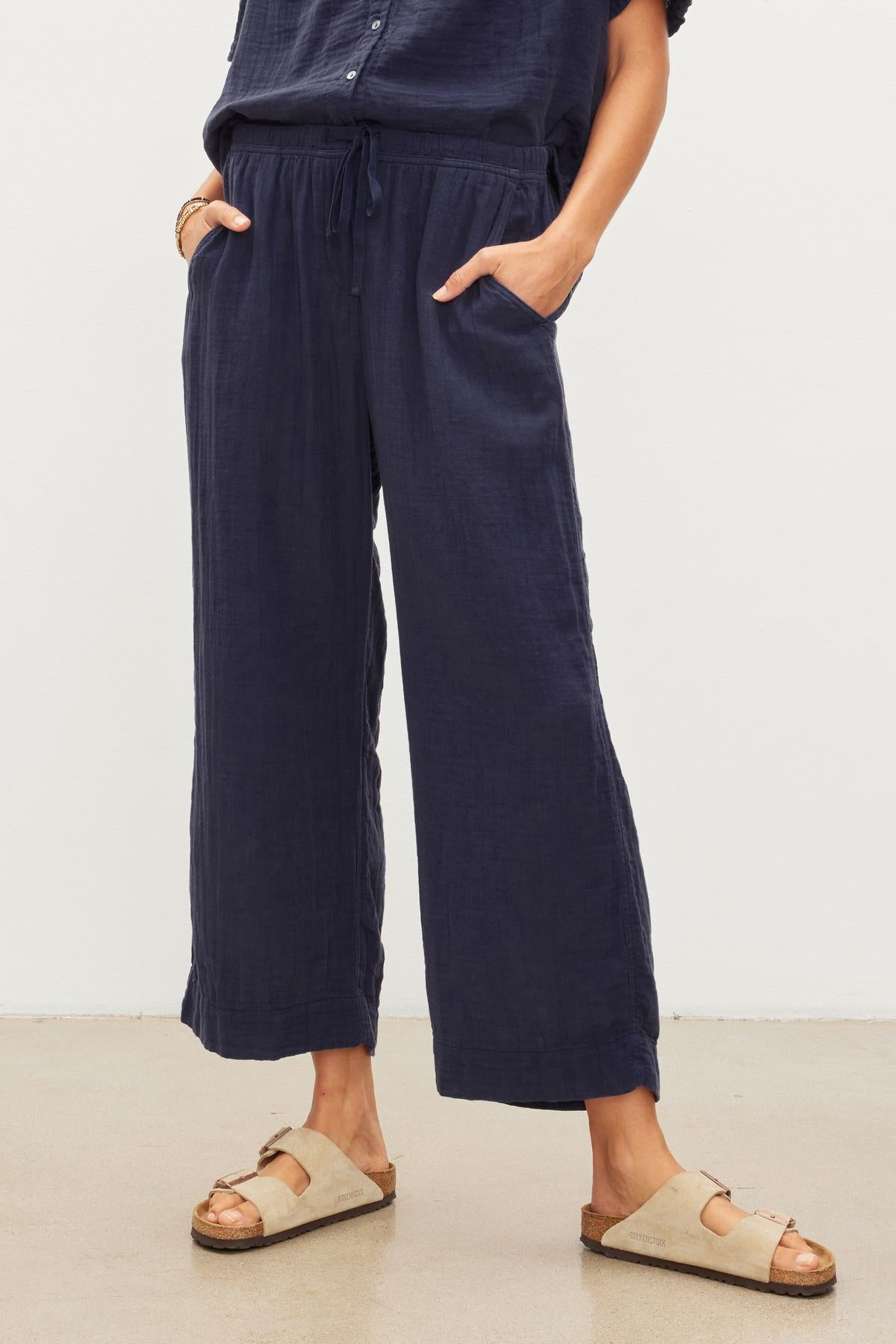 Woman standing in navy blue FRANNY COTTON GAUZE drawstring pants from Velvet by Graham & Spencer with relaxed leg and beige sandals.-36443730149569