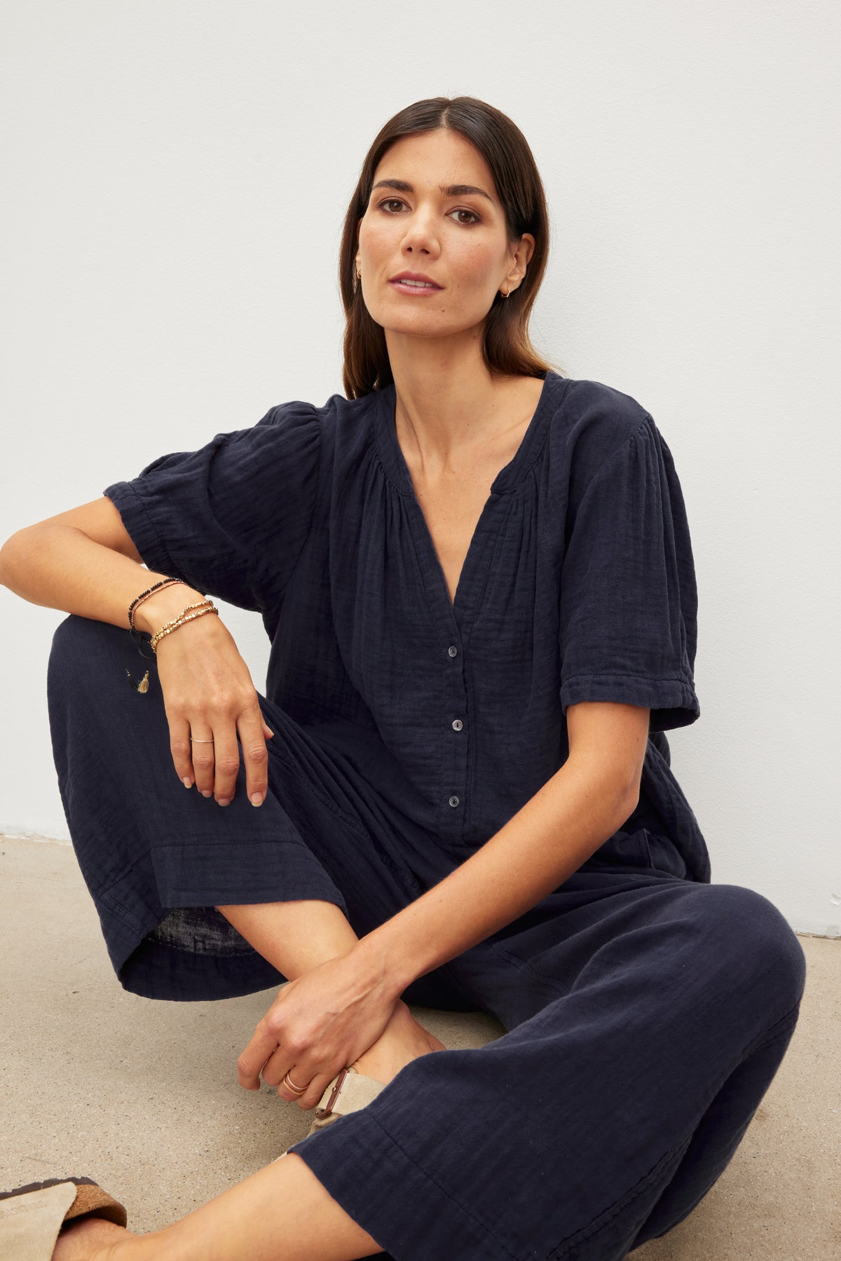 Woman in a casual navy blue outfit featuring FRANNY COTTON GAUZE PANTS by Velvet by Graham & Spencer with relaxed legs, sitting against a neutral background.-36443734016193