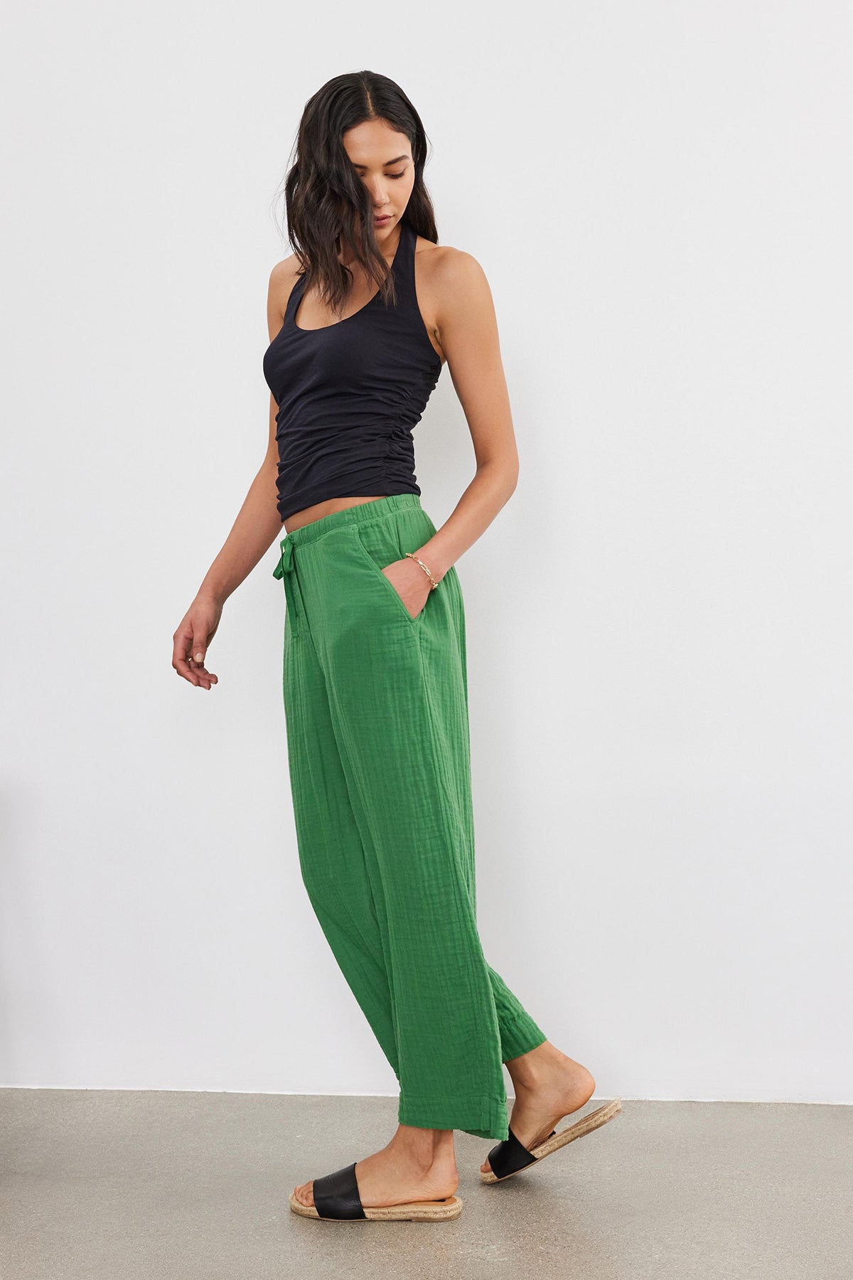 A woman in a black tank top and Velvet by Graham & Spencer Franny Cotton Gauze Pants with relaxed legs stands against a plain background, her hand resting on her hip.-36917078425793