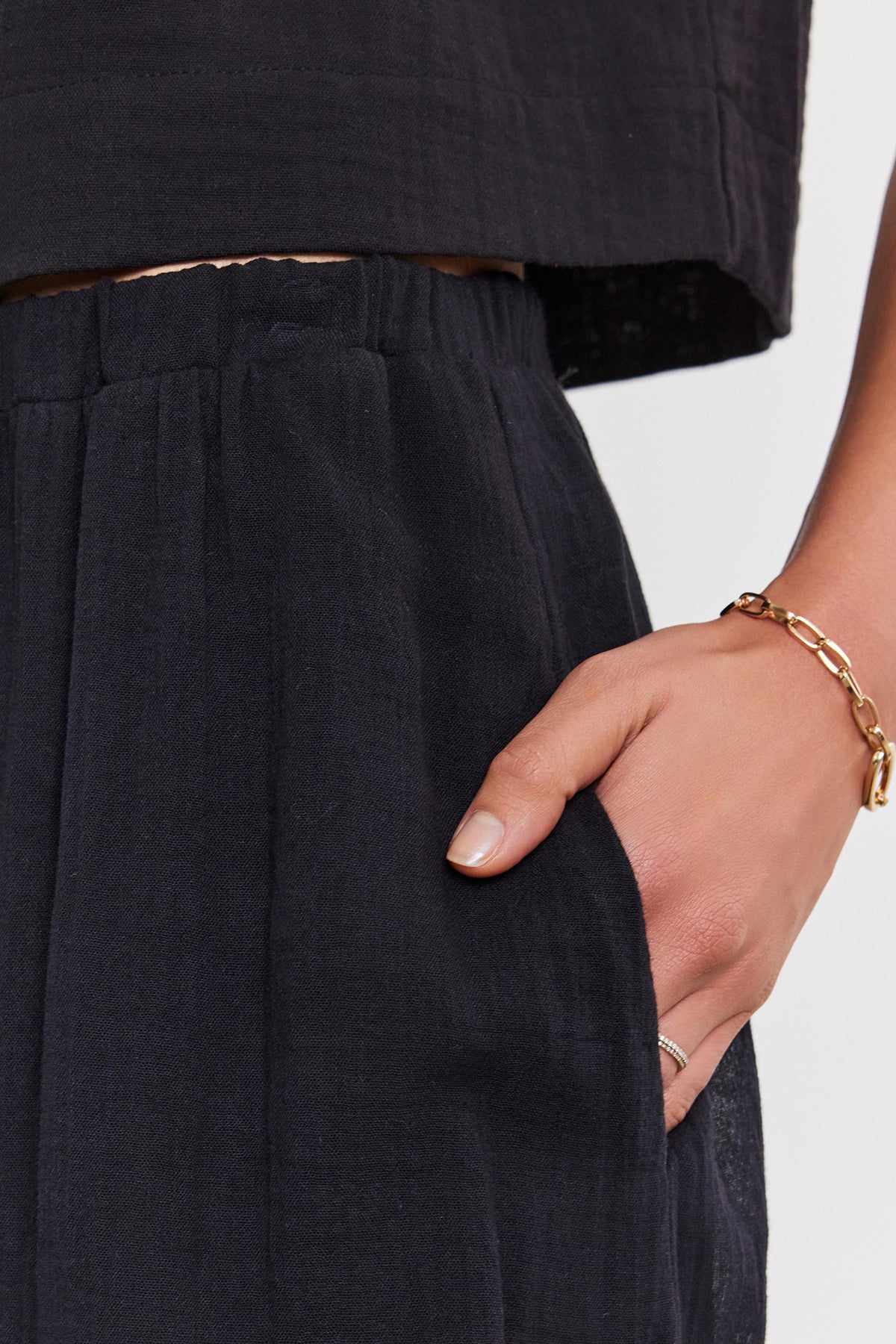   Close-up of a woman's hand with a gold bracelet and rings, resting on her Velvet by Graham & Spencer INDY COTTON GAUZE SKIRT. 