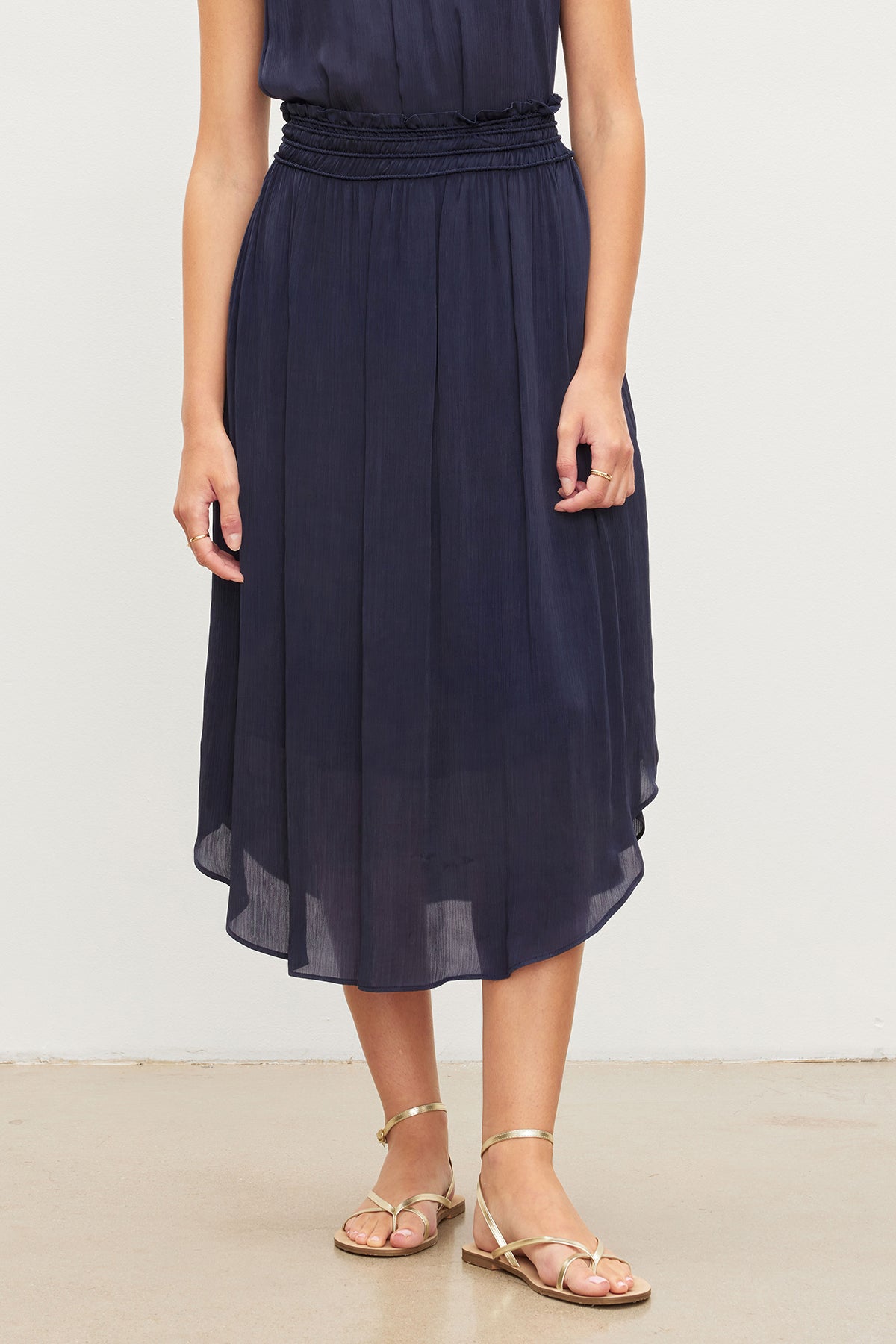   Woman wearing a navy blue DIMI SMOCKED SKIRT with inseam pockets and gold sandals by Velvet by Graham & Spencer. 