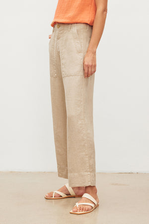 A person standing in a Velvet by Graham & Spencer DRU HEAVY LINEN PANT with patch pockets and white sandals against a plain background.