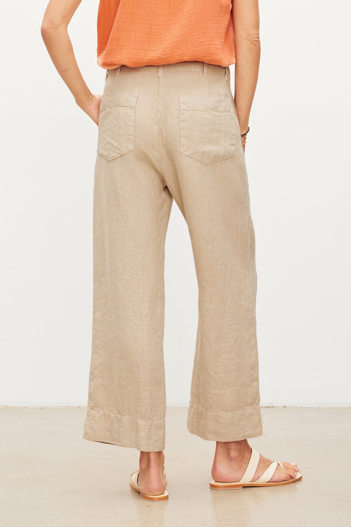 Person standing in a neutral pose wearing Velvet by Graham & Spencer DRU Heavy Linen Pant with patch pockets and light-colored sandals, with a partial view of an orange top.-36247918543041
