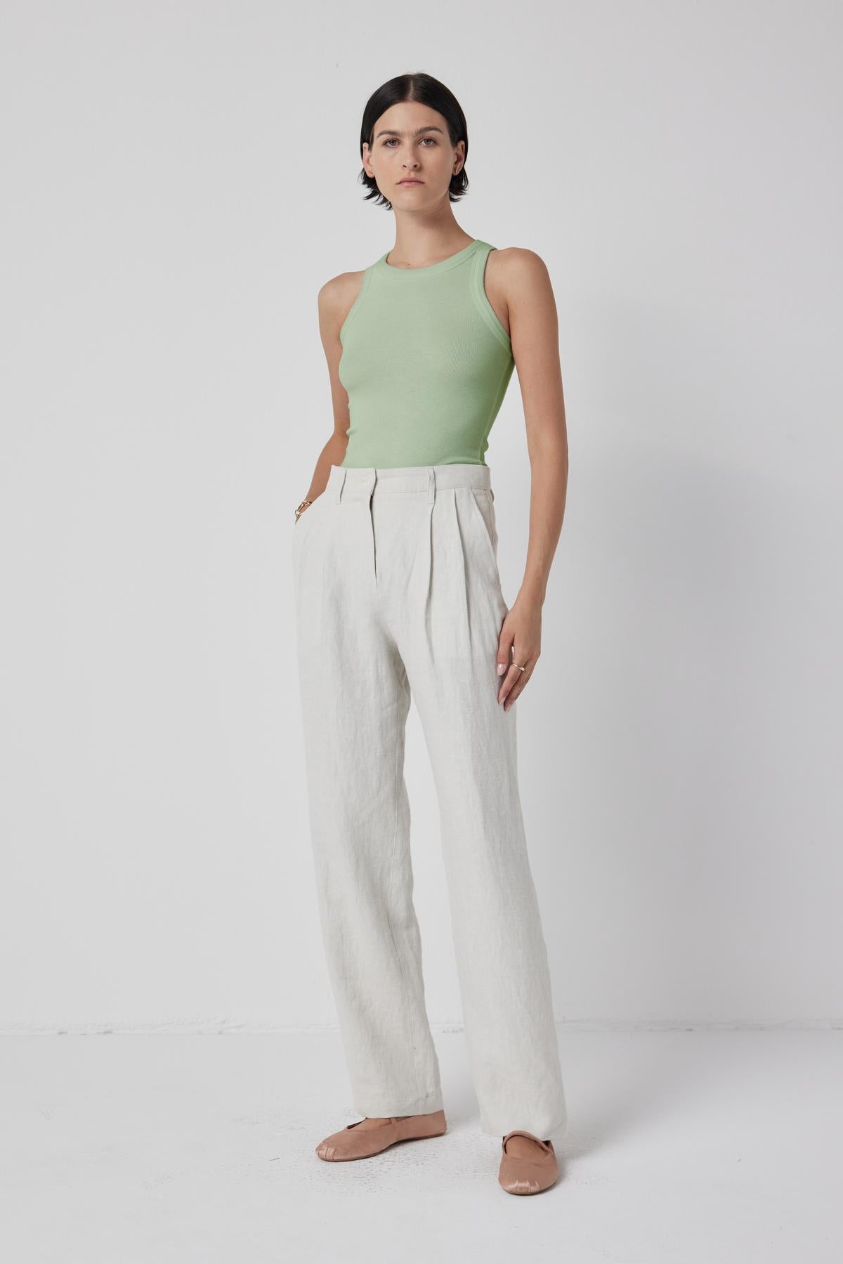 The model is wearing a green CRUZ tank top and white linen pants that showcase her toned body by Velvet by Jenny Graham.-36198188024001