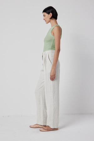 The model is wearing a Cruz Tank Top by Velvet by Jenny Graham and white linen pants that stretch comfortably over the body.