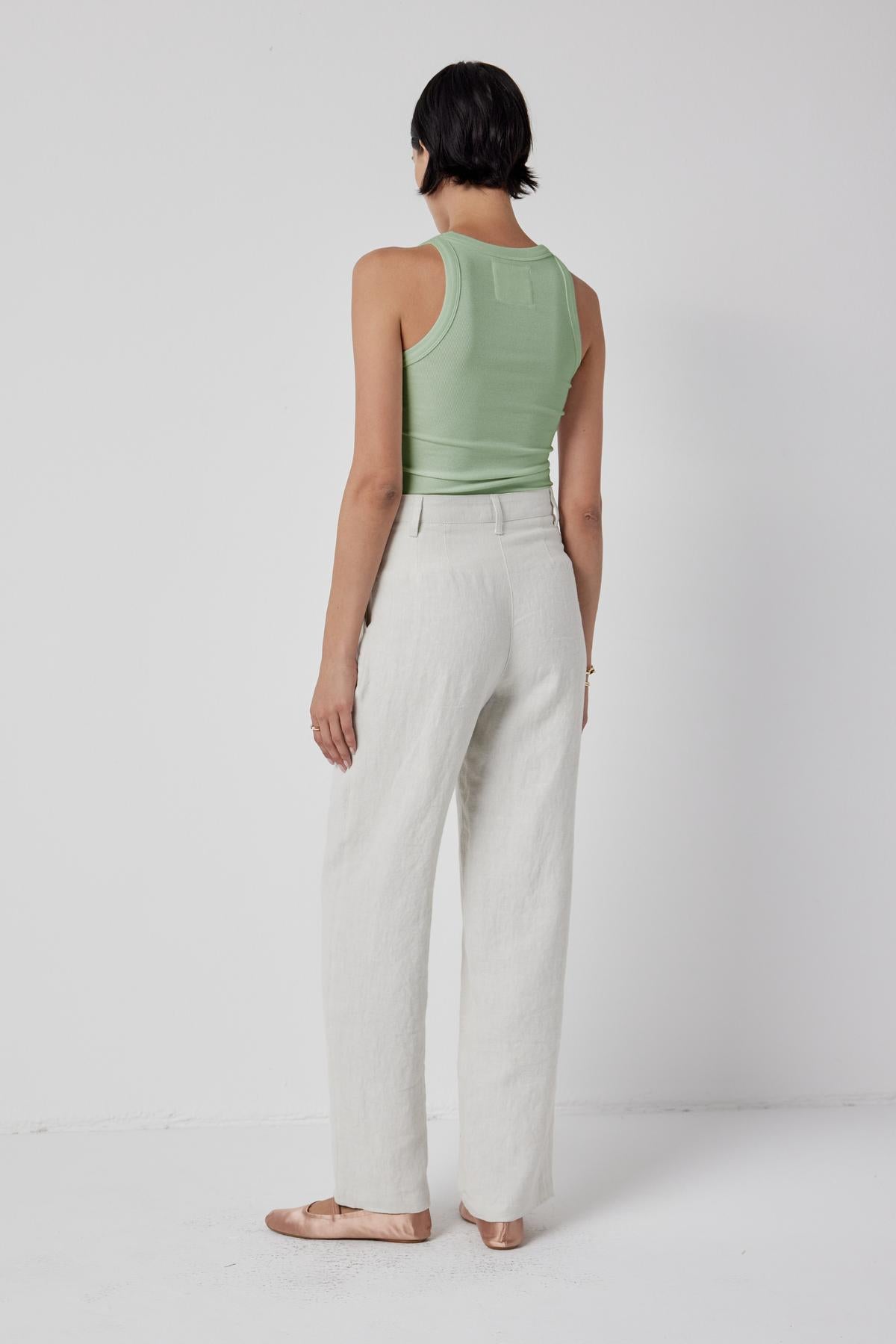 The back view of a woman wearing linen pants and a CRUZ tank top by Velvet by Jenny Graham, showcasing her toned body.-36198187991233
