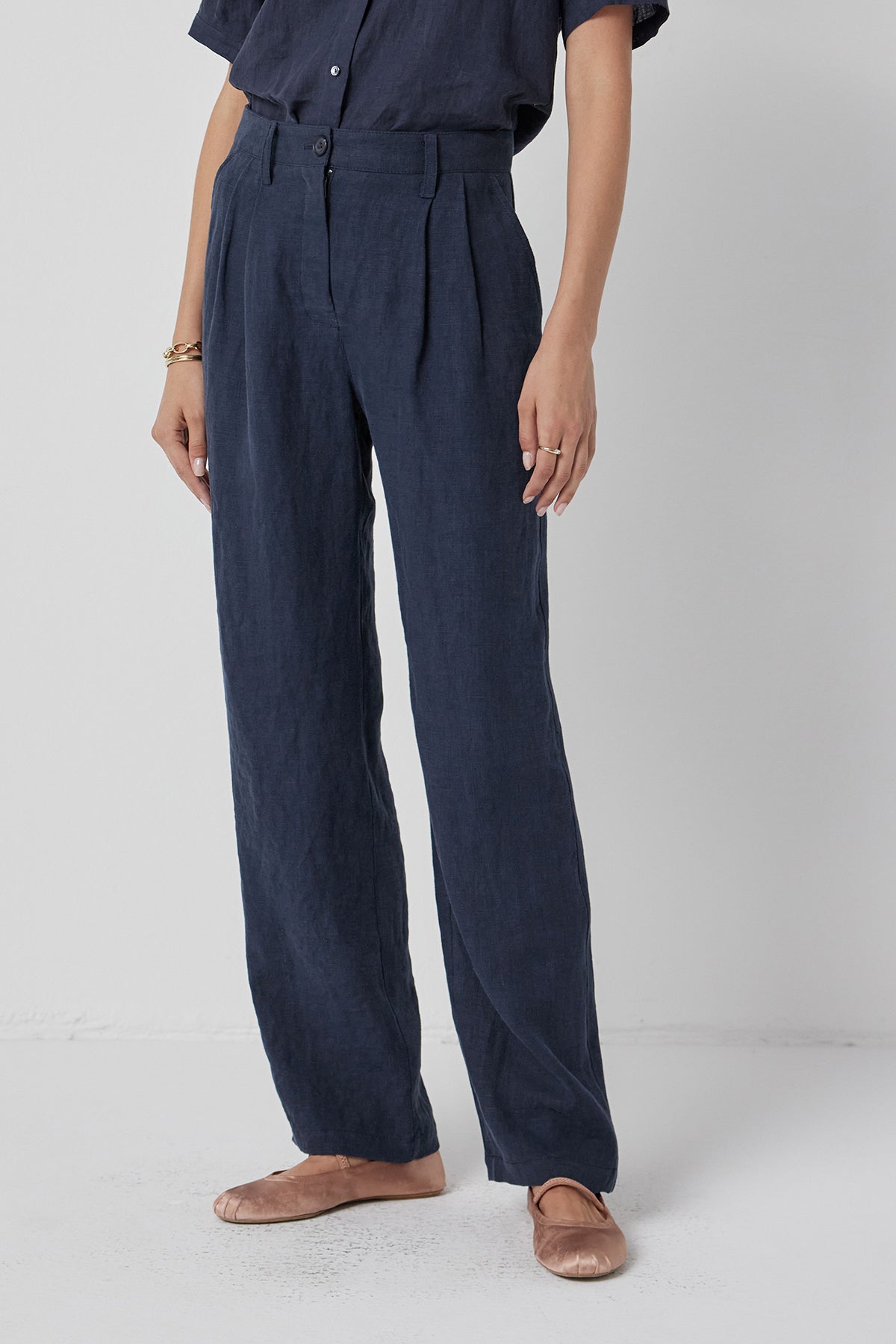 A person wearing Velvet by Jenny Graham's POMONA PANT, a heavy-weight linen, dark blue jumpsuit paired with brown shoes, standing against a white background.-36409575669953