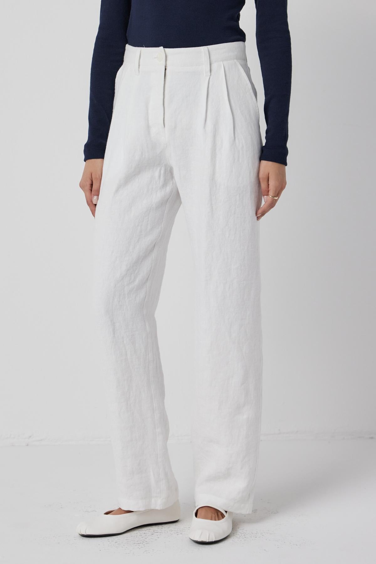 A person standing in Velvet by Jenny Graham's POMONA PANT - white straight-leg linen trousers with pockets, paired with a dark top and white flat shoes.-36463685959873