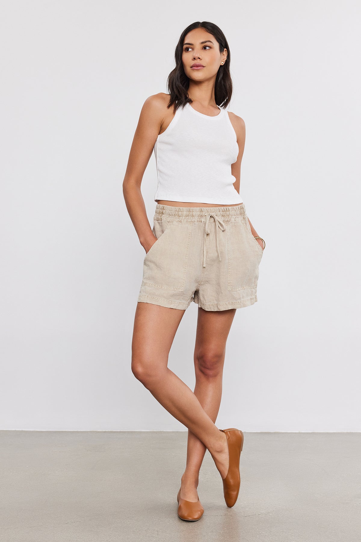   A woman in a white tank top and Velvet by Graham & Spencer SUTTON HEAVY LINEN SHORT stands confidently against a neutral background. 