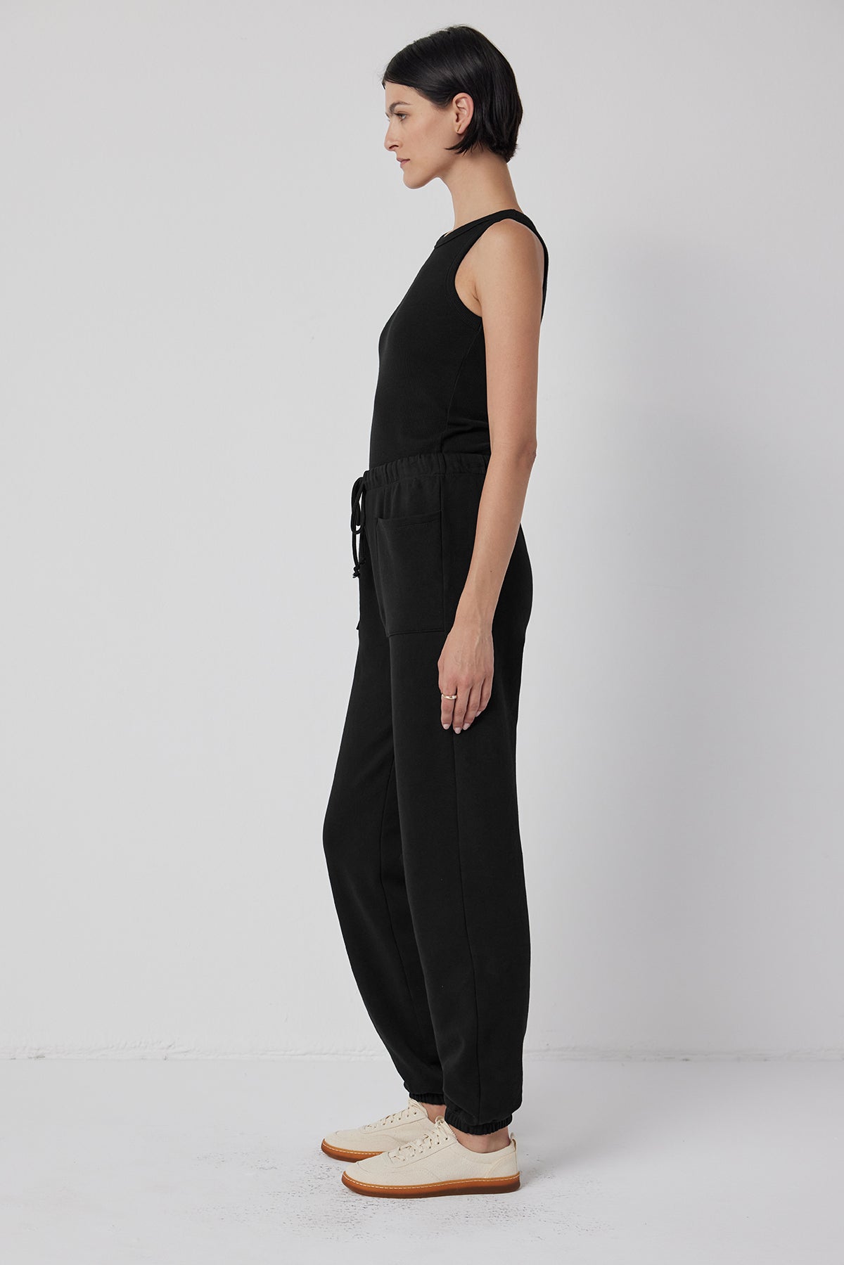 Person in a WESTLAKE SWEATPANT by Velvet by Jenny Graham, paired with a black sleeveless jumpsuit featuring an elastic drawstring waist, and white shoes, standing sideways against a plain white background.-38208768901313