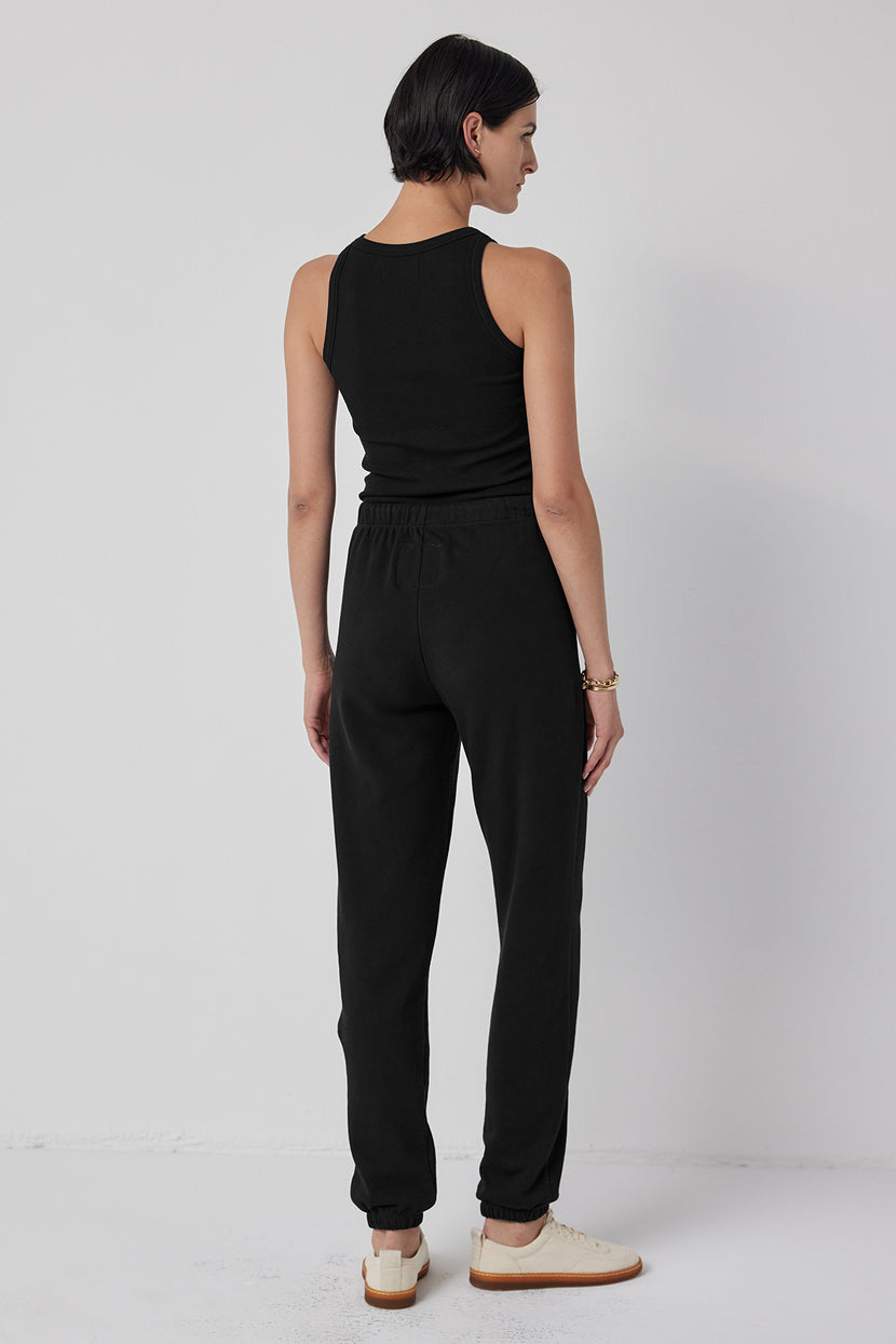 Viewed against a gray background, a person wears the WESTLAKE SWEATPANT by Velvet by Jenny Graham—a stylish pair of joggers made from organic cotton fleece with an elastic drawstring waist—and a black tank top.