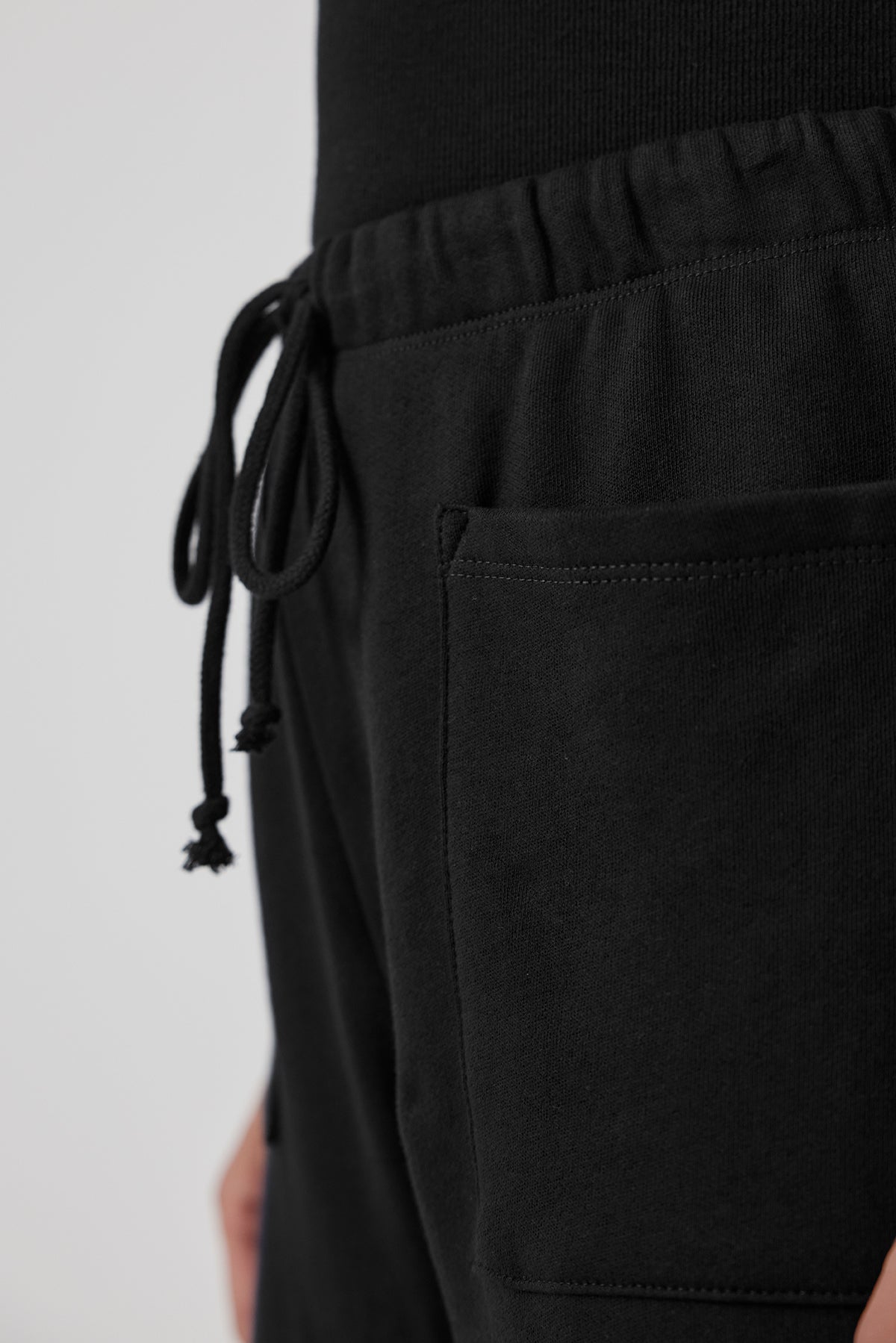   Close-up of the WESTLAKE SWEATPANT by Velvet by Jenny Graham, made from black organic cotton fleece, featuring an elastic drawstring waist and a convenient side pocket. 