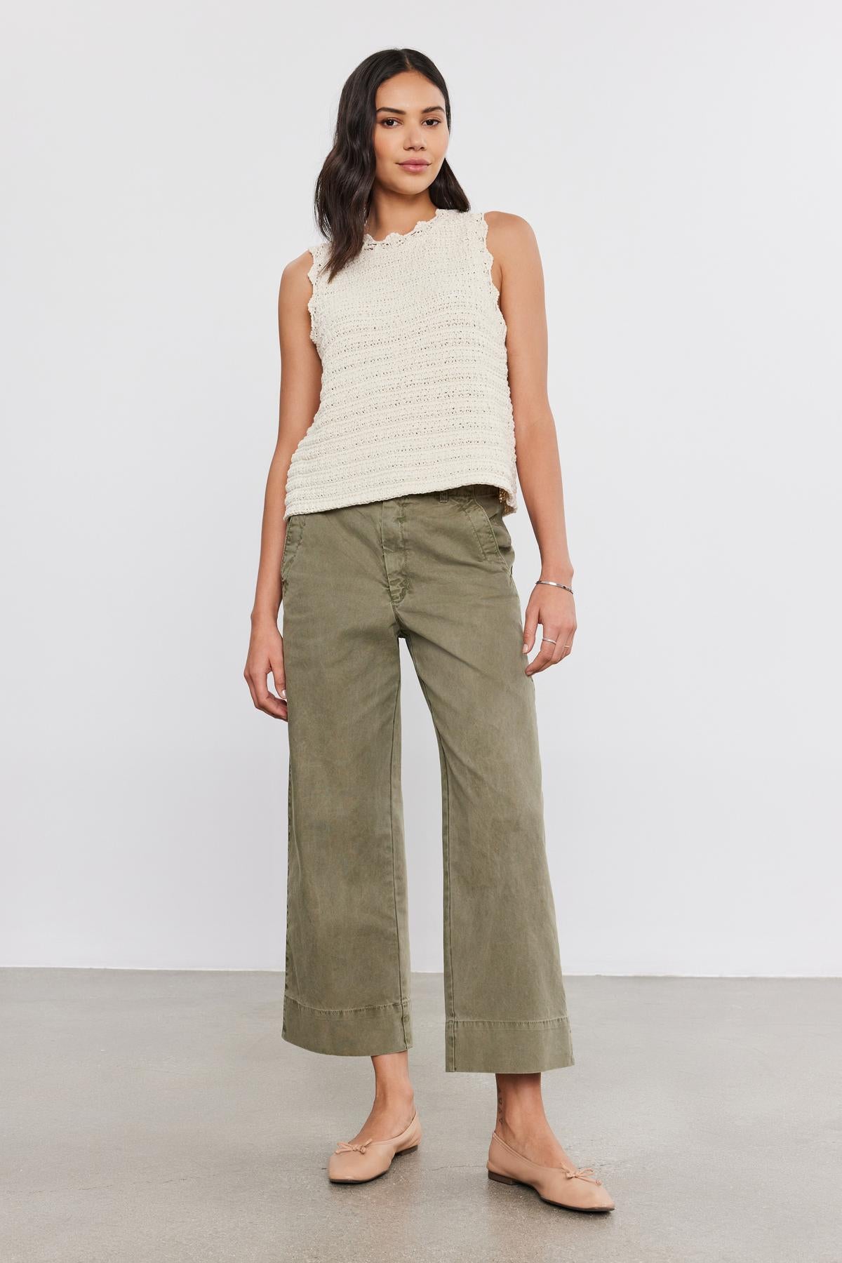   A woman stands against a plain white background wearing a sleeveless beige top, the versatile fit Sabine Cotton Canvas Pant by Velvet by Graham & Spencer in olive green with a wide-leg design, and beige flats. 