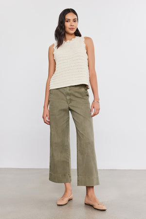 A woman stands against a plain white background wearing a sleeveless beige top, the versatile fit Sabine Cotton Canvas Pant by Velvet by Graham & Spencer in olive green with a wide-leg design, and beige flats.