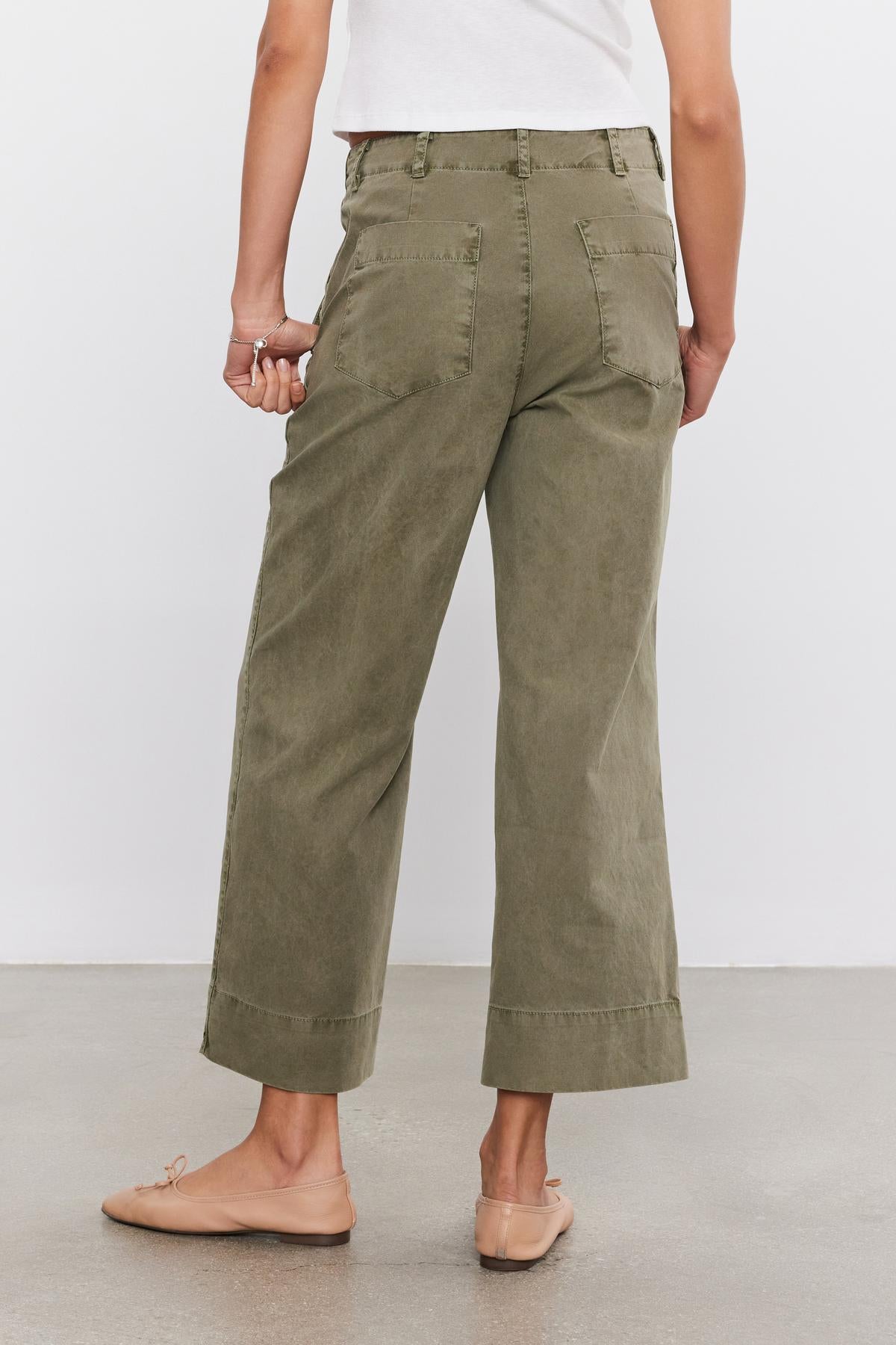 Person wearing olive green "Sabine Cotton Canvas Pant" by Velvet by Graham & Spencer, a white top, and nude flats, standing on a concrete floor, photographed from the back.-37934979711169