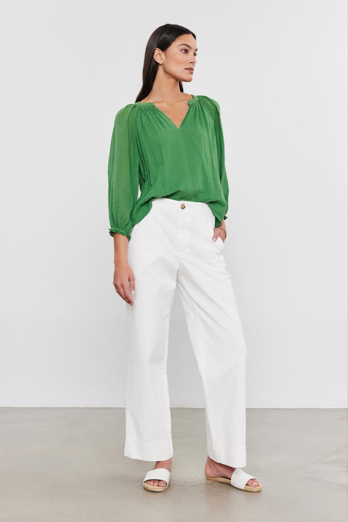   Person wearing a green long-sleeved blouse, versatile-fit Velvet by Graham & Spencer SABINE cotton canvas pants, and white sandals, standing against a plain background. 