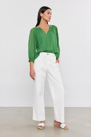 Person wearing a green long-sleeved blouse, versatile-fit Velvet by Graham & Spencer SABINE cotton canvas pants, and white sandals, standing against a plain background.