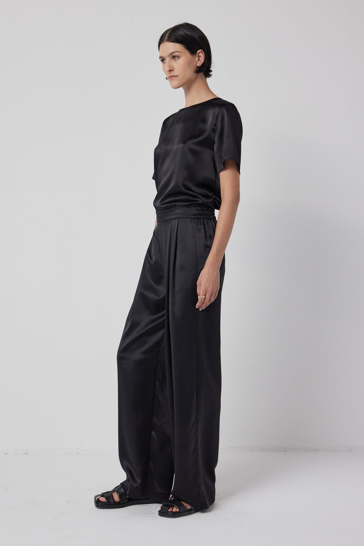   A woman stands in profile wearing a Velvet by Jenny Graham Pasadena Top and wide-leg trousers, paired with black sandals, against a plain background. 