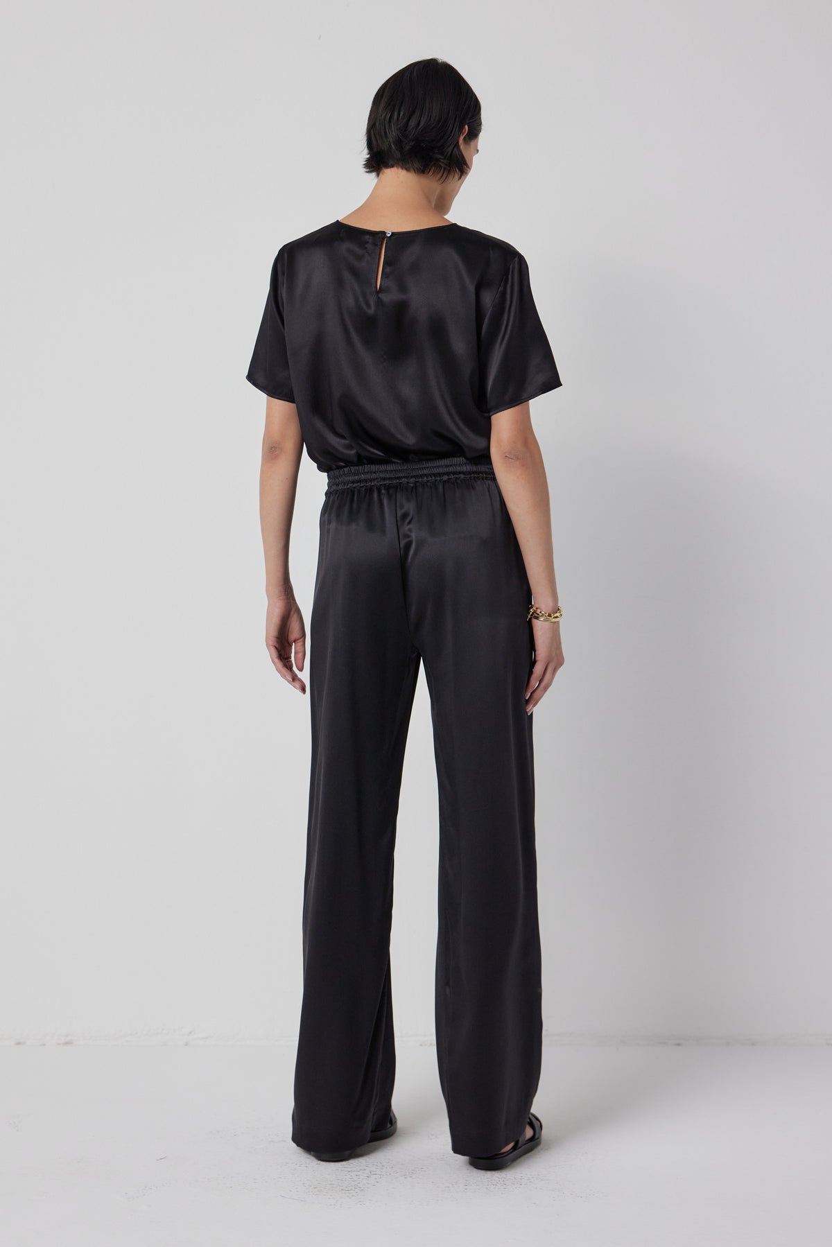   Woman from behind wearing a black silk charmeuse PASADENA TOP and matching trousers by Velvet by Jenny Graham, exuding timeless elegance. 