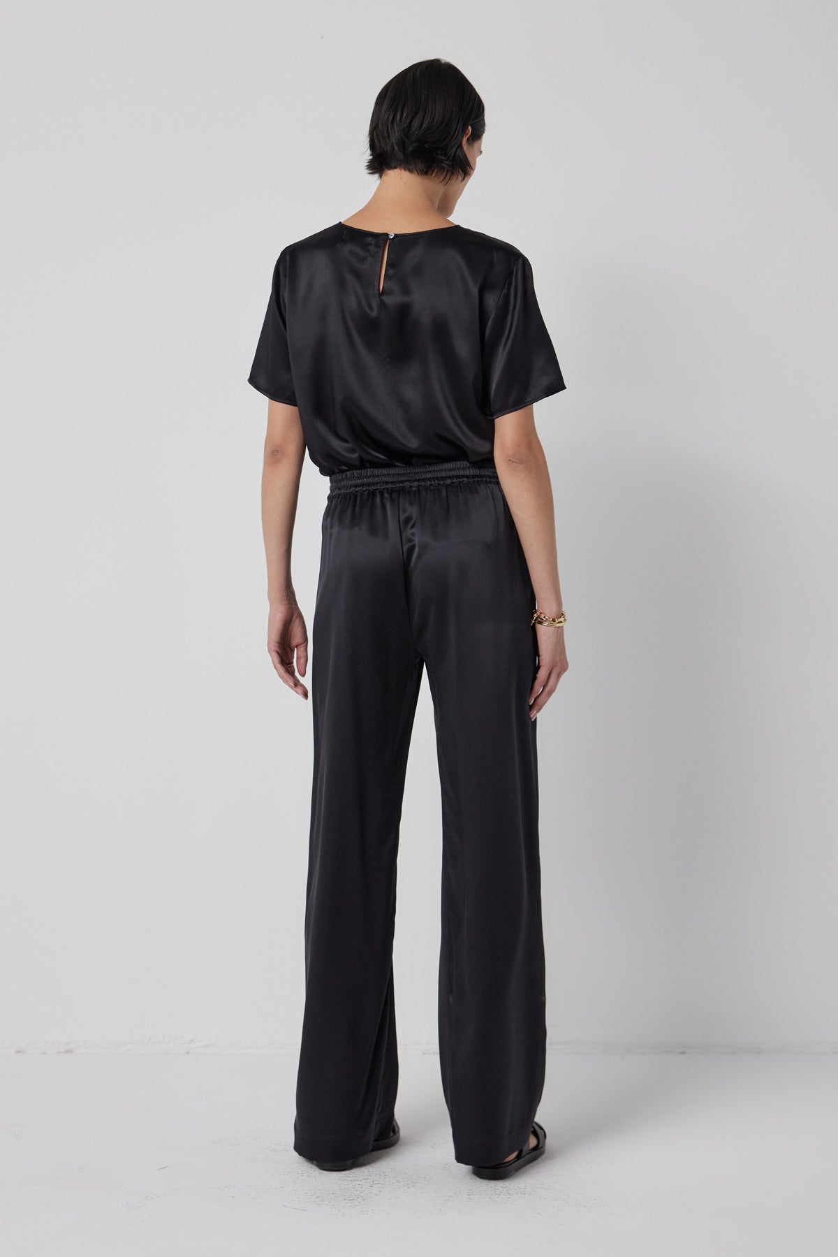 Woman from behind wearing a black silk charmeuse PASADENA TOP and matching trousers by Velvet by Jenny Graham, exuding timeless elegance.-36463793832129
