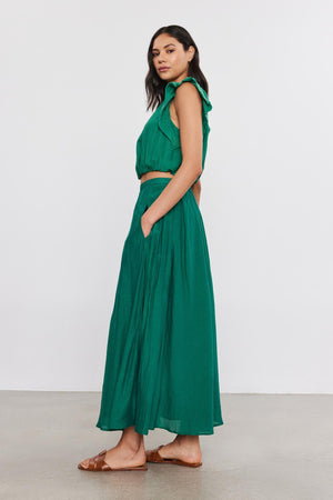 Woman in a green sleeveless lined Mariela skirt and brown sandals, standing sideways, looking over her shoulder against a neutral background.