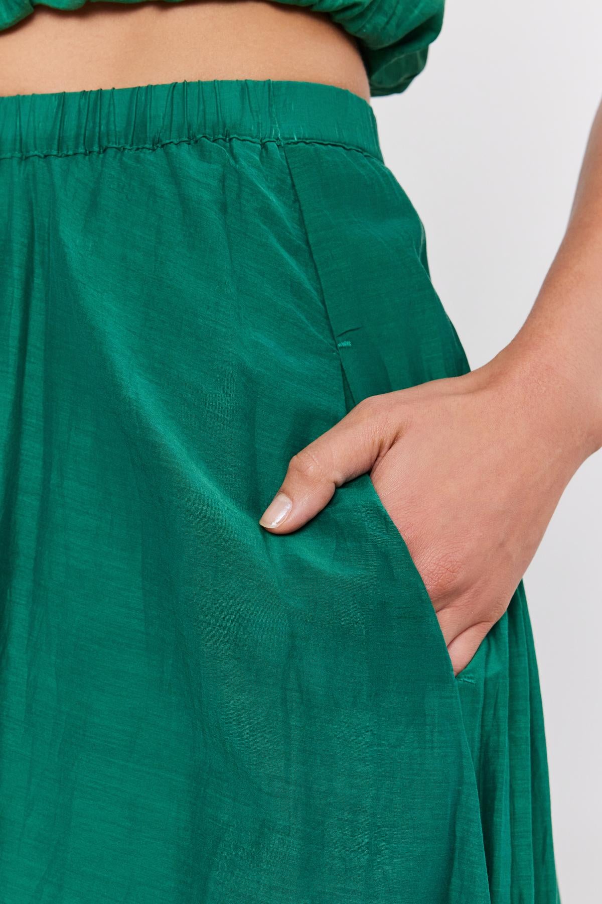   Close-up of a hand with pale pink nail polish, tugging at the pocket of a Velvet by Graham & Spencer MARIELA SKIRT. 