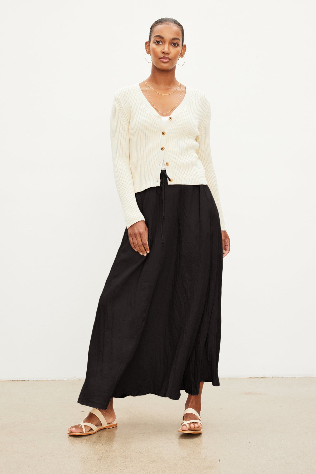 A person stands against a white background wearing a cream sweater, Velvet by Graham & Spencer BAILEY LINEN MAXI SKIRT with an elastic drawstring waist, and sandals.-37240025743553