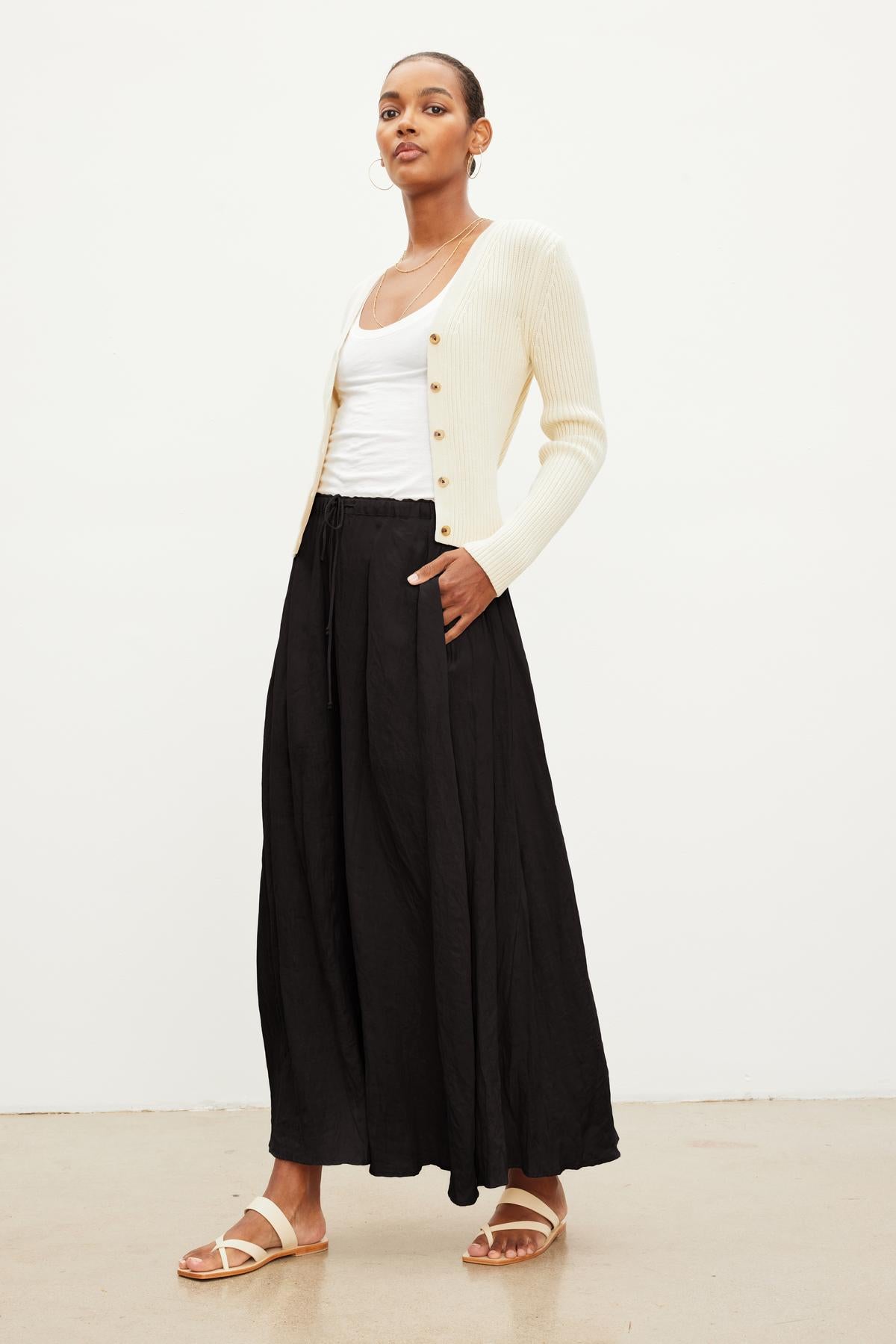 Woman posing in a white ribbed cardigan over a white tank top with a BAILEY LINEN MAXI SKIRT by Velvet by Graham & Spencer featuring an elastic drawstring waist, and beige sandals against a plain white background.-37240025776321