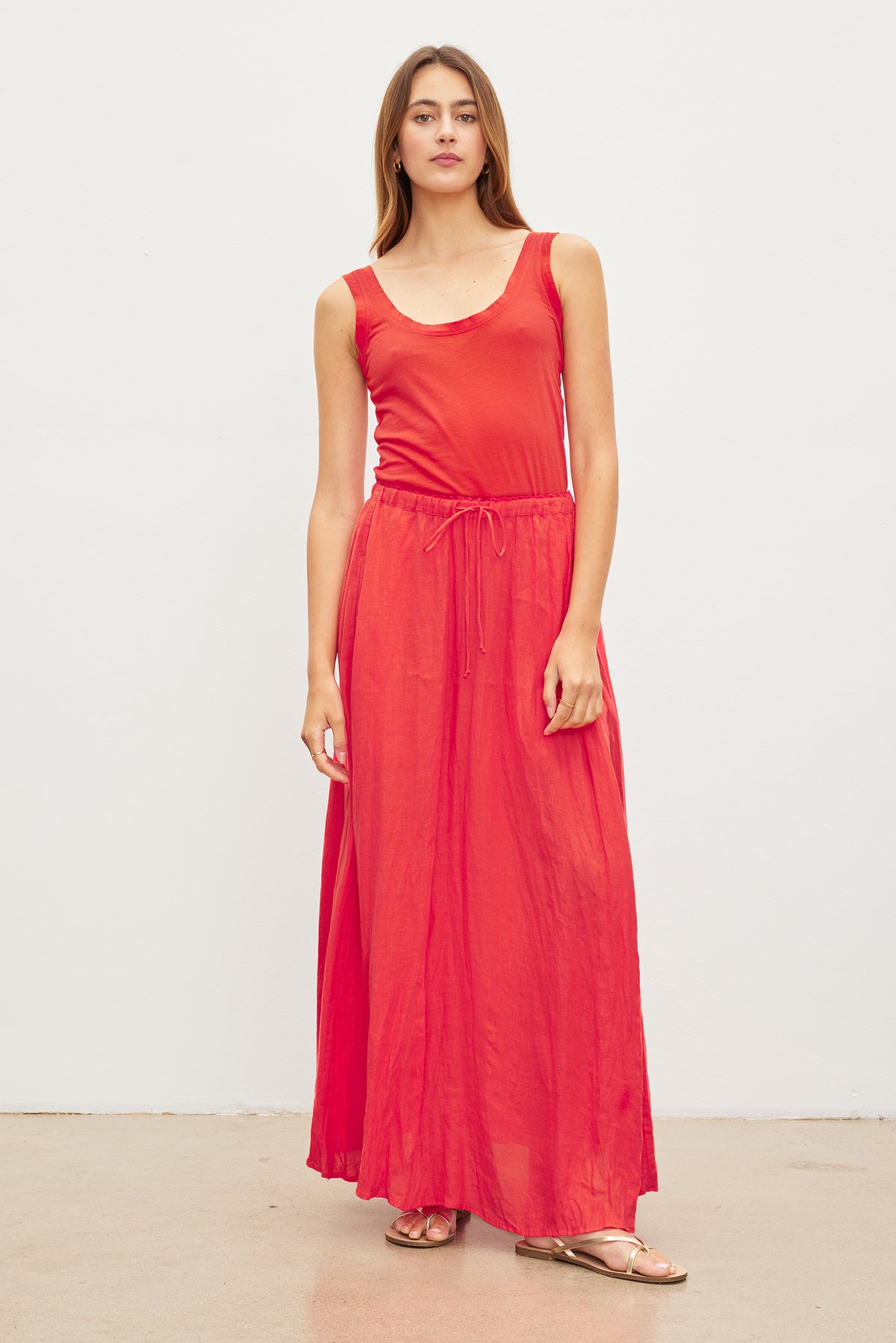   A woman donning the Velvet by Graham & Spencer BAILEY LINEN MAXI SKIRT, a stunning red maxi dress made from woven linen fabric, featuring an elegant elastic drawstring waist for added comfort and style. 