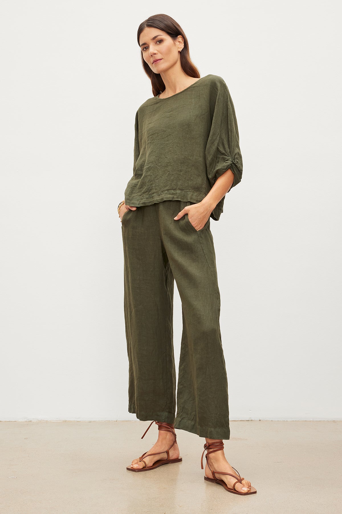 A person wears a loose-fitting dark green CASS LINEN TOP with a twist knot from Velvet by Graham & Spencer, paired with wide-legged pants and brown sandals.-35955522961601