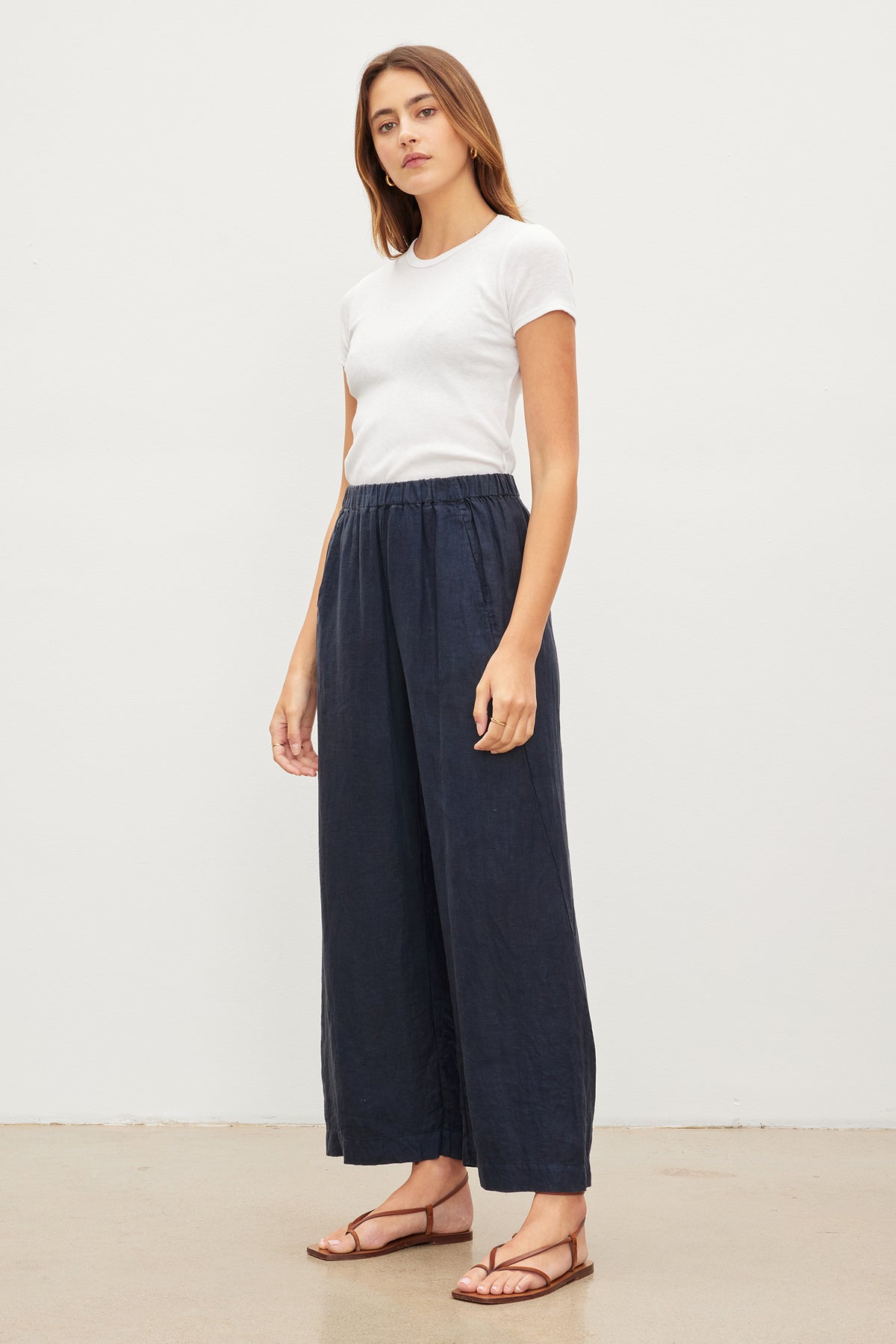 Woman standing in a studio, wearing a white t-shirt and Velvet by Graham & Spencer LOLA LINEN PANT with an elastic waist and tan sandals.-36581077450945