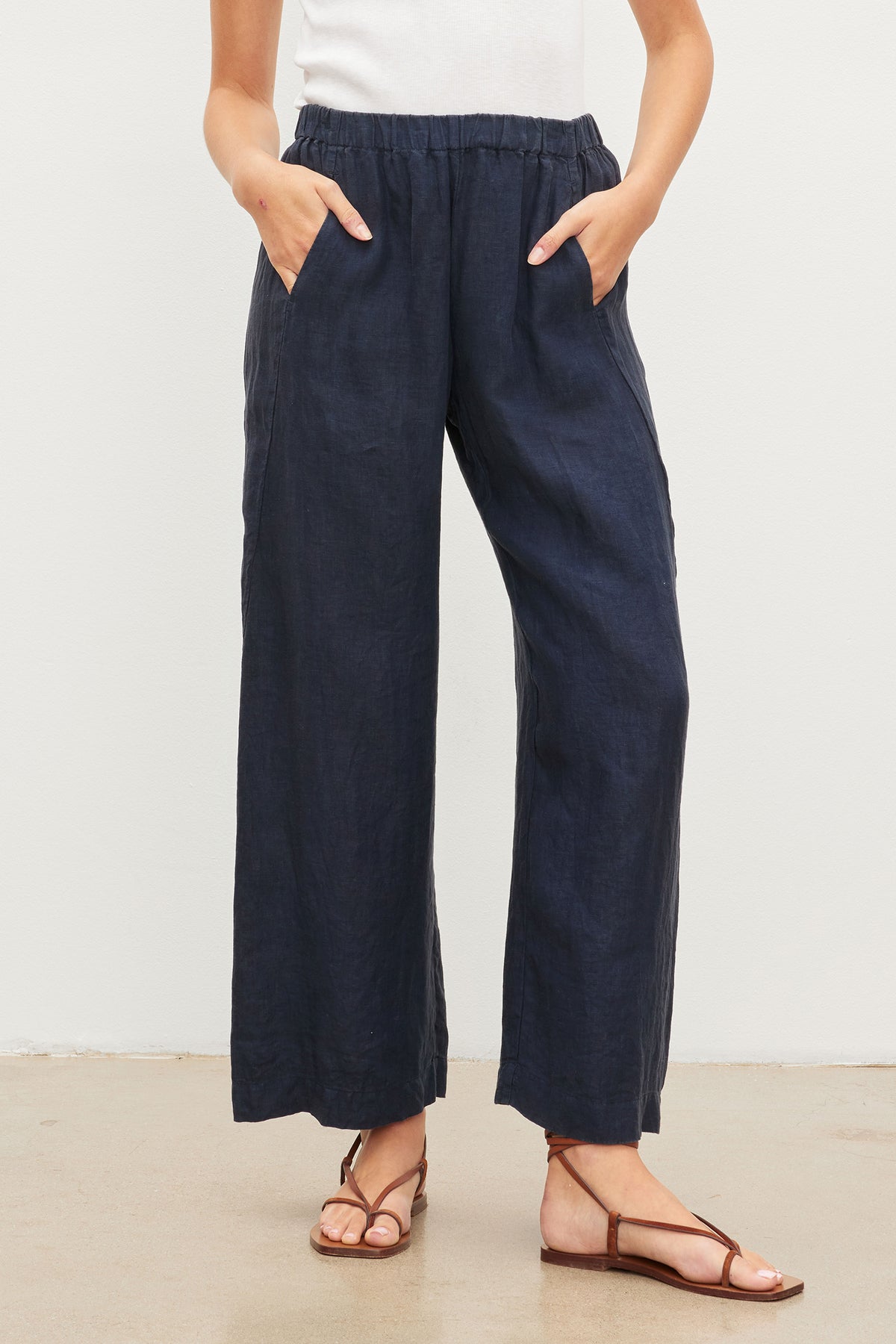   Person standing in LOLA LINEN PANT from Velvet by Graham & Spencer with an elastic waist, paired with metallic strap sandals on a neutral background. 
