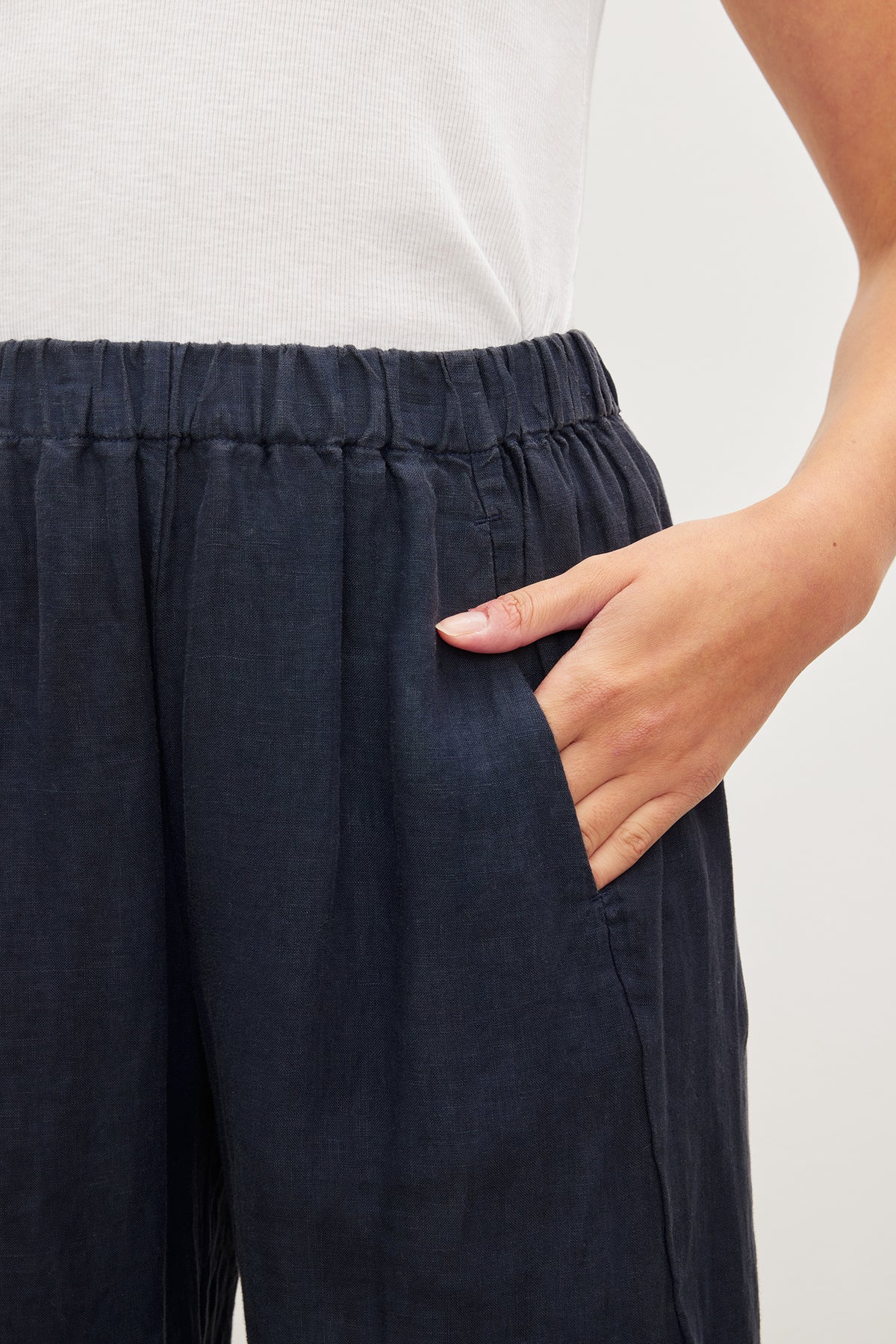   Close-up of a person's hand tucking into the pocket of dark blue Velvet by Graham & Spencer LOLA LINEN PANT. 