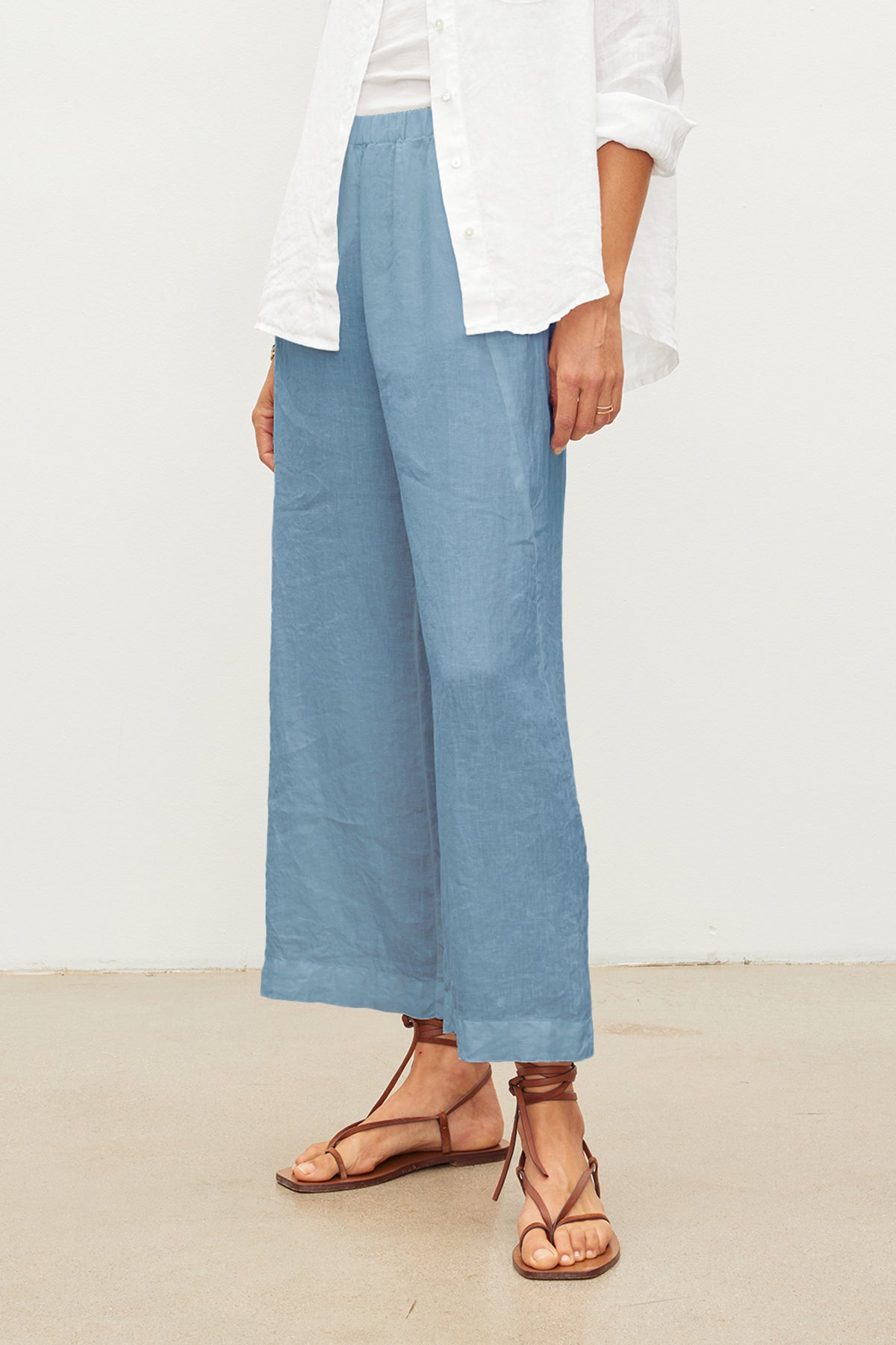 A person is wearing light blue LOLA LINEN PANT by Velvet by Graham & Spencer, a white shirt, and brown sandals against a plain background.-36161404928193