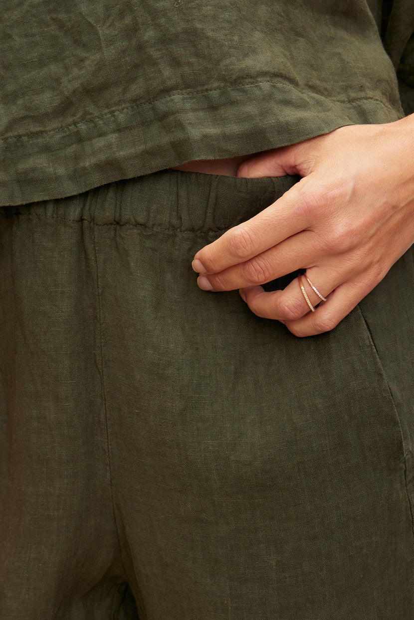 Close-up of a hand with a ring, tucking into the pocket of Velvet by Graham & Spencer's LOLA LINEN PANT.