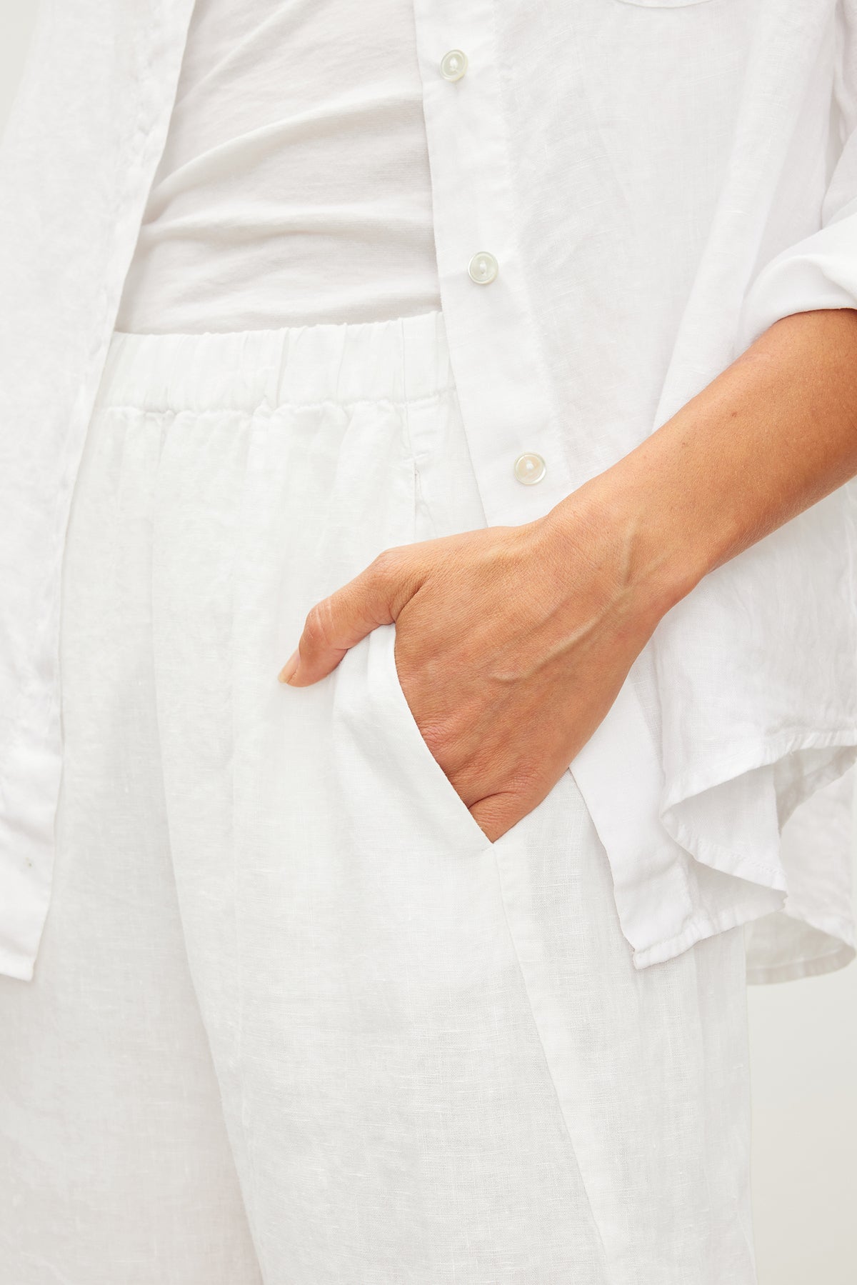 A person wearing a white outfit has their hand in the pocket of Velvet by Graham & Spencer's LOLA LINEN PANT. The photo is cropped from the shoulders to the thighs.-36161692696769