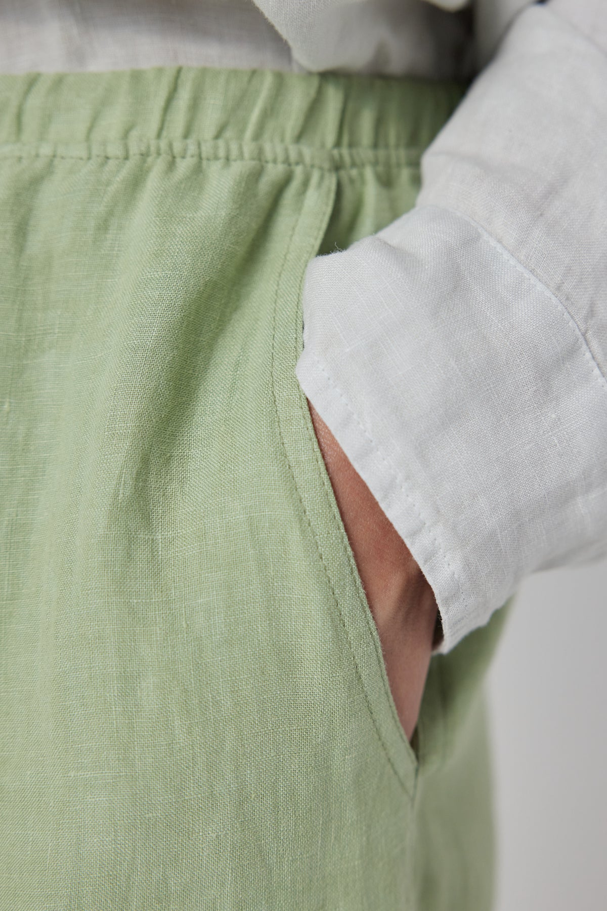   Close-up of a person wearing Velvet by Jenny Graham's PICO LINEN PANT in green, with a white shirt partially tucked in, focusing on the elastic waist and fabric detail. 