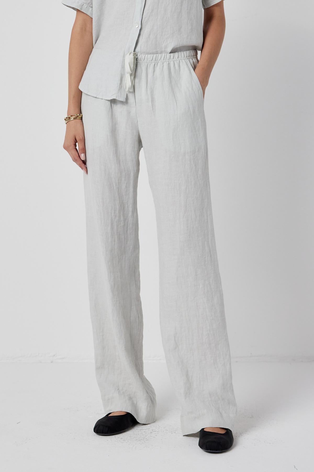   The model is wearing Velvet by Jenny Graham's PICO PANT, a relaxed fit linen pants with an elastic waistband, and a white shirt. 