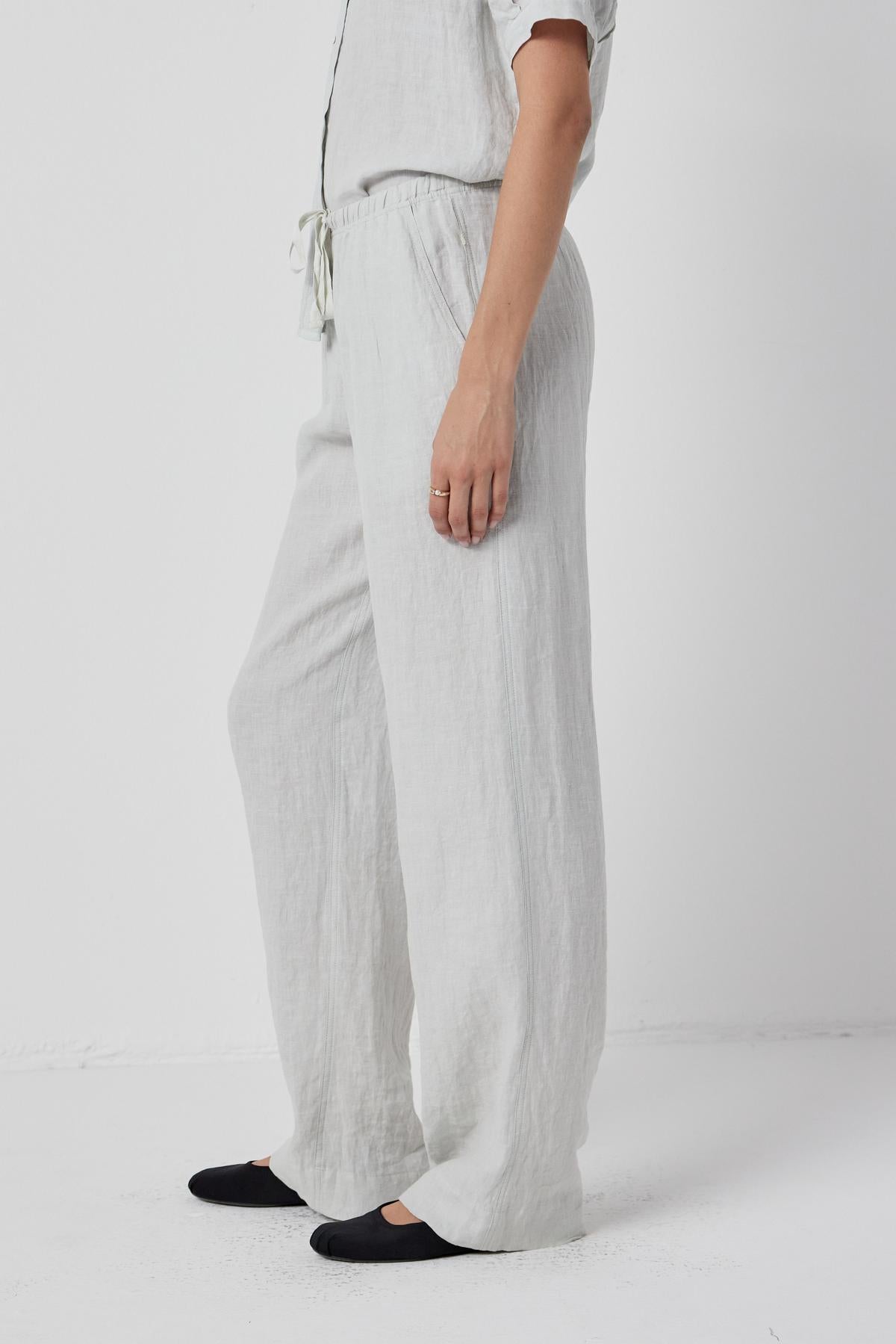   The model is dressed in a relaxed fit white linen PICO PANT jumpsuit with elastic waist by Velvet by Jenny Graham. 