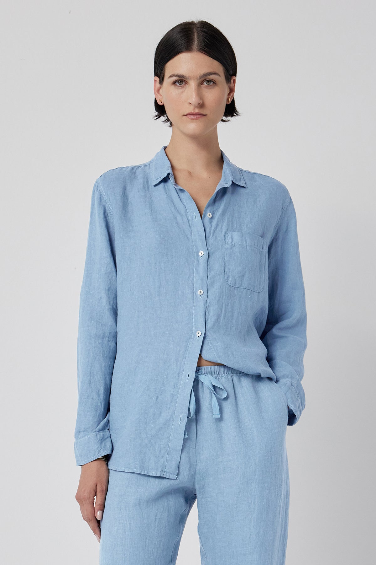   A woman wearing a blue linen Mulholland Shirt by Velvet by Jenny Graham with a relaxed silhouette and scooped hemline. 