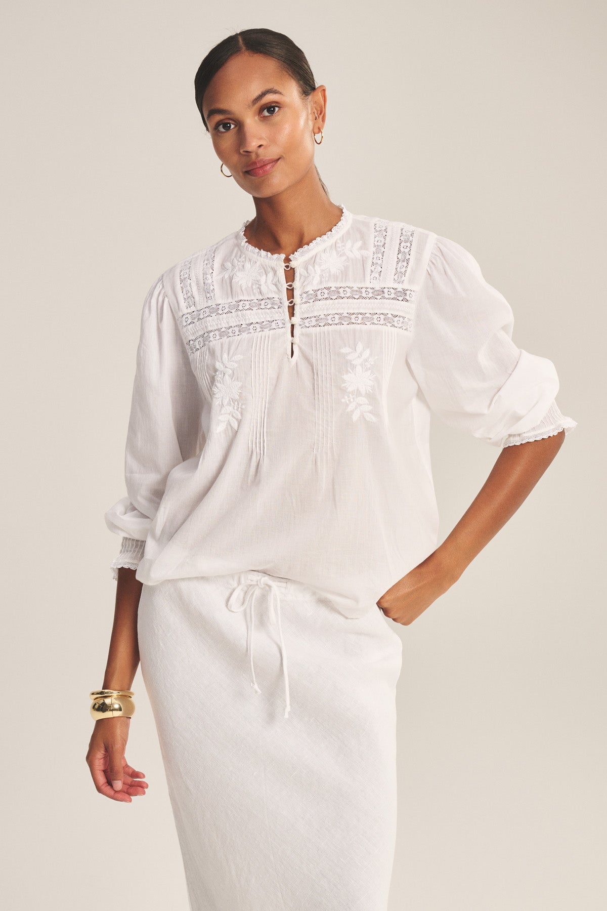 A woman wears the BYRDIE TOP by Velvet by Graham & Spencer—a white, long-sleeve embroidered blouse with a front keyhole—paired with a matching skirt, standing against a neutral background.-41128031322305