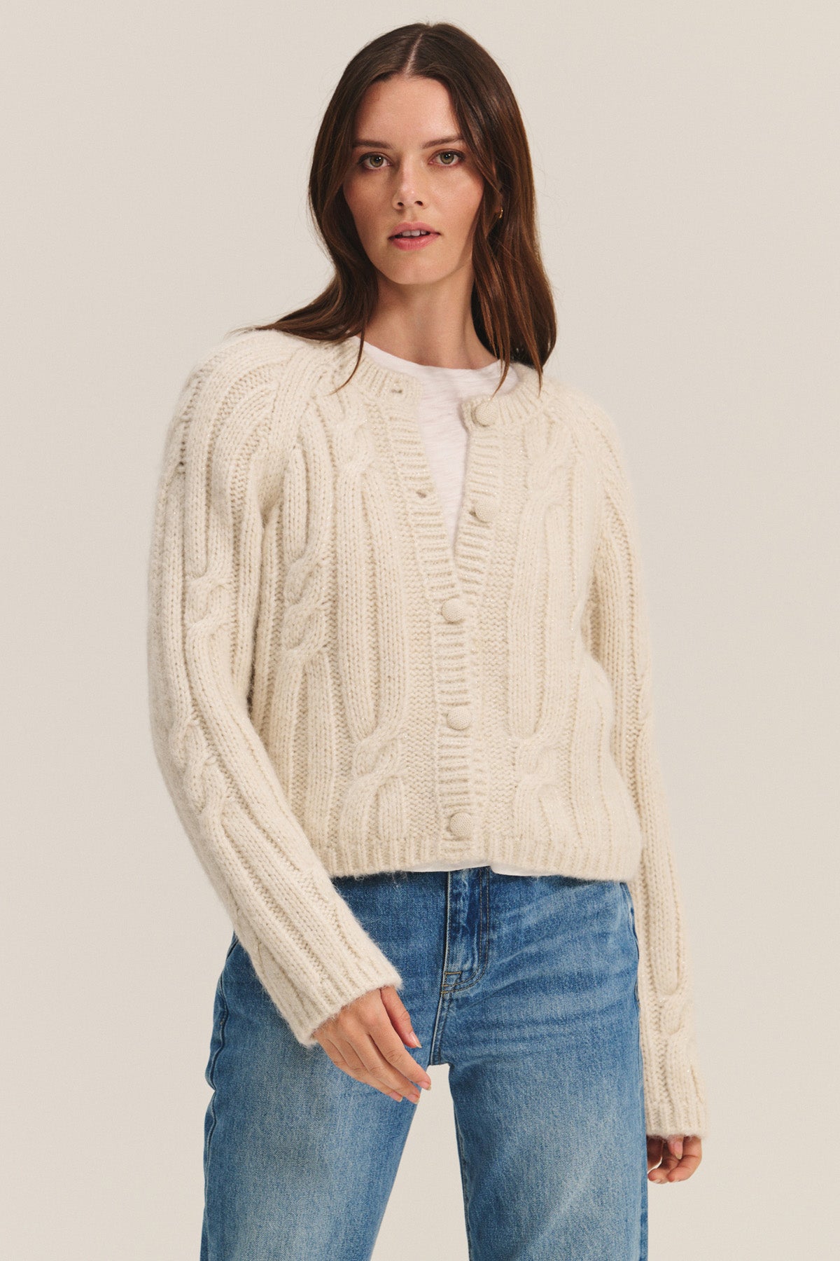 A woman in the ALLISON CARDIGAN by Velvet by Graham & Spencer, layered over a white shirt and blue jeans, stands against a plain background.