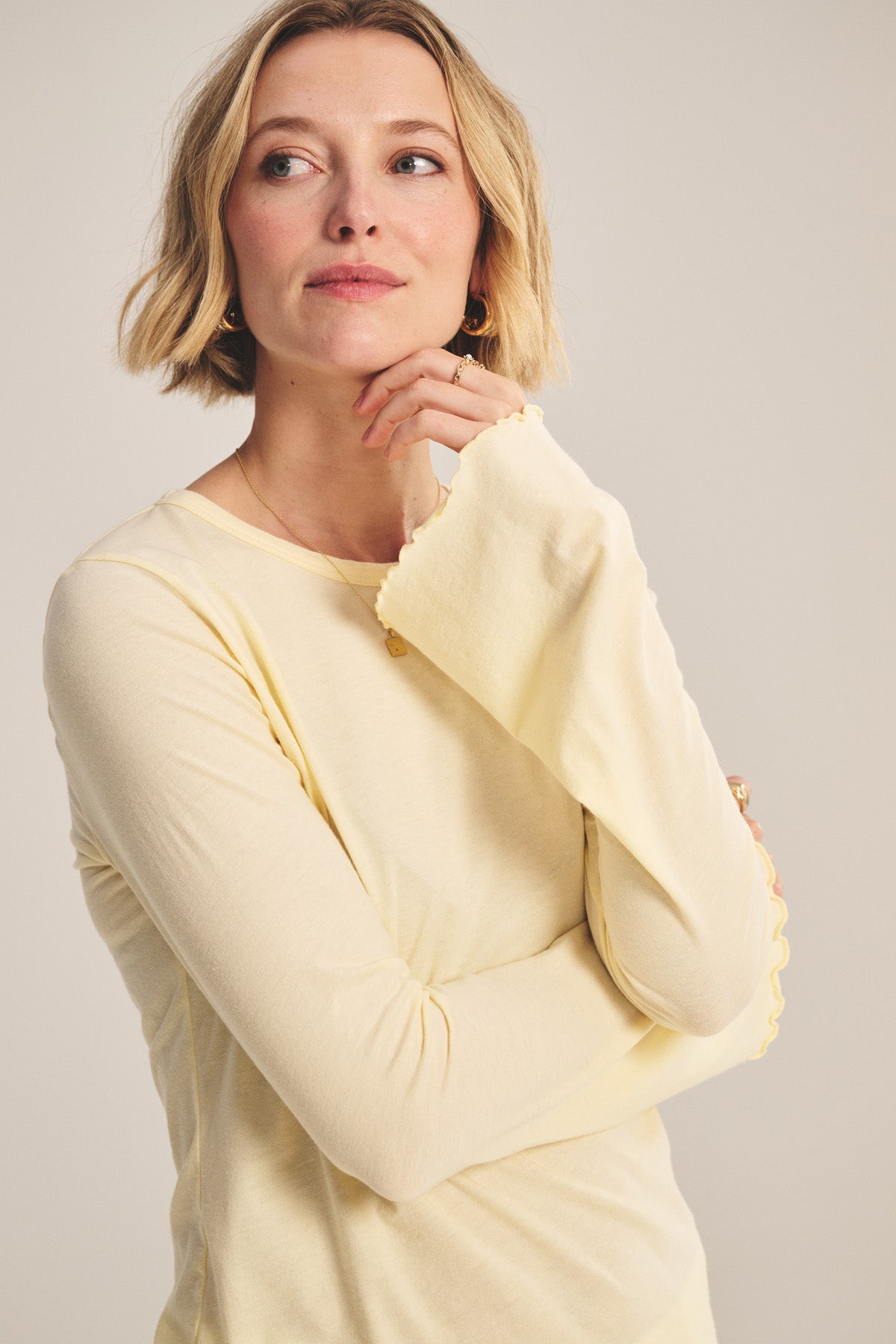 A woman with short blonde hair wears the CAMILLE TEE by Velvet by Graham & Spencer in light yellow, looking slightly to the side with her hand resting near her chin.