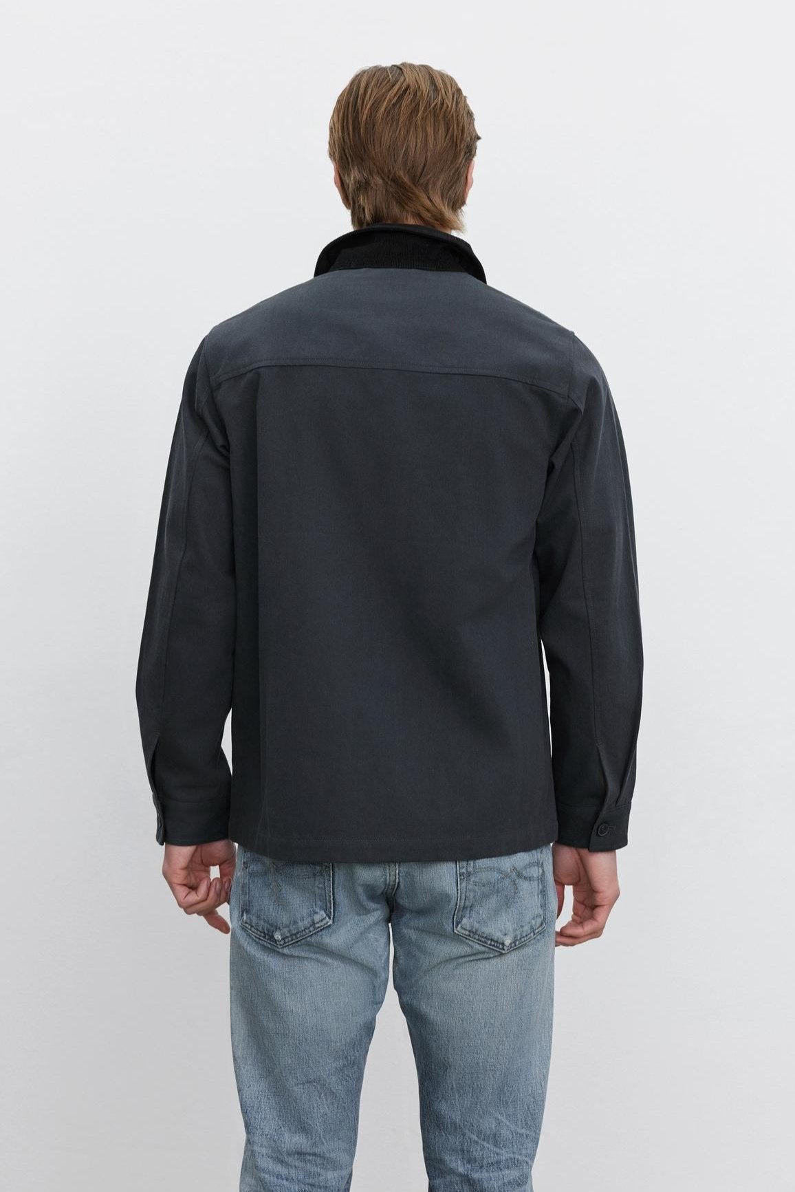   A person with brown hair, seen from the back, wearing the EMORY JACKET by Velvet by Graham & Spencer in dark blue structured cotton canvas and light blue jeans against a plain white background. 